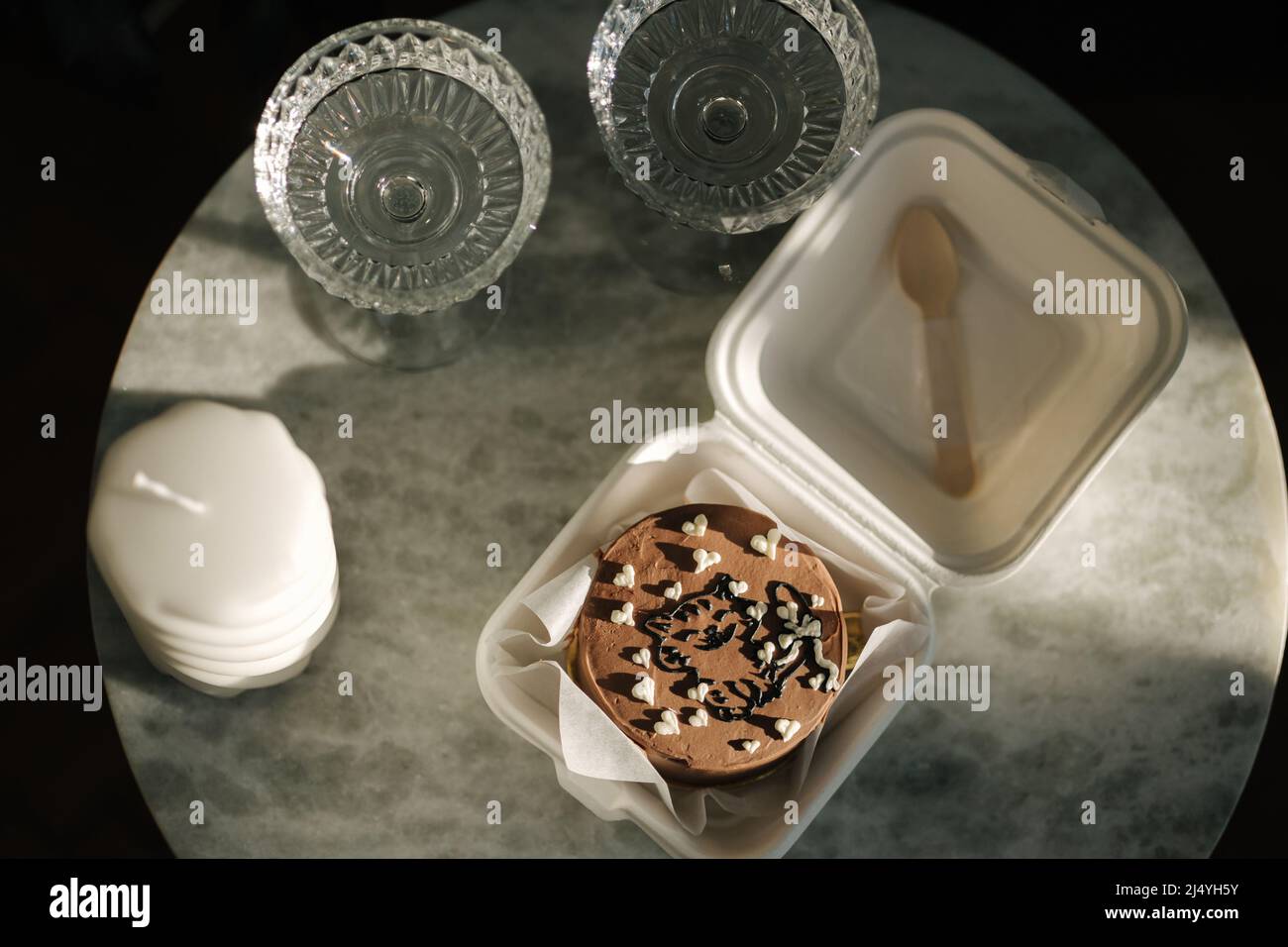 Top view of Chocolate bento cake in eco box with wooden spoon. White candle and chmpagne glasses on luxury marble table Stock Photo