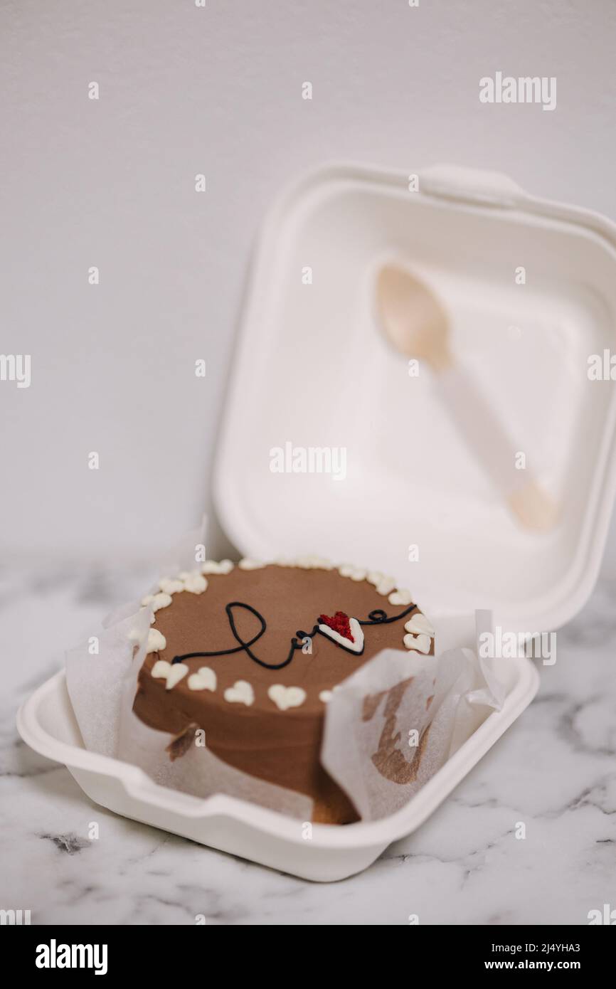 Bento cake with inscription love and white sugar hearts in eco box-packaging with wooden spoon. Chocolate cake Stock Photo