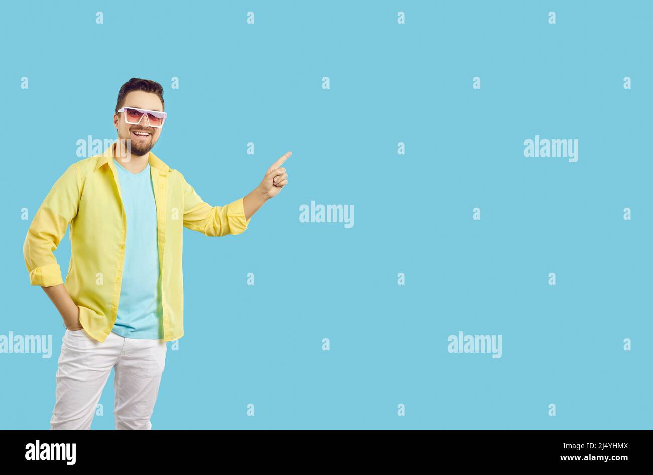 Happy man in casual summer clothes and sunglasses pointing to copy space on blue background Stock Photo
