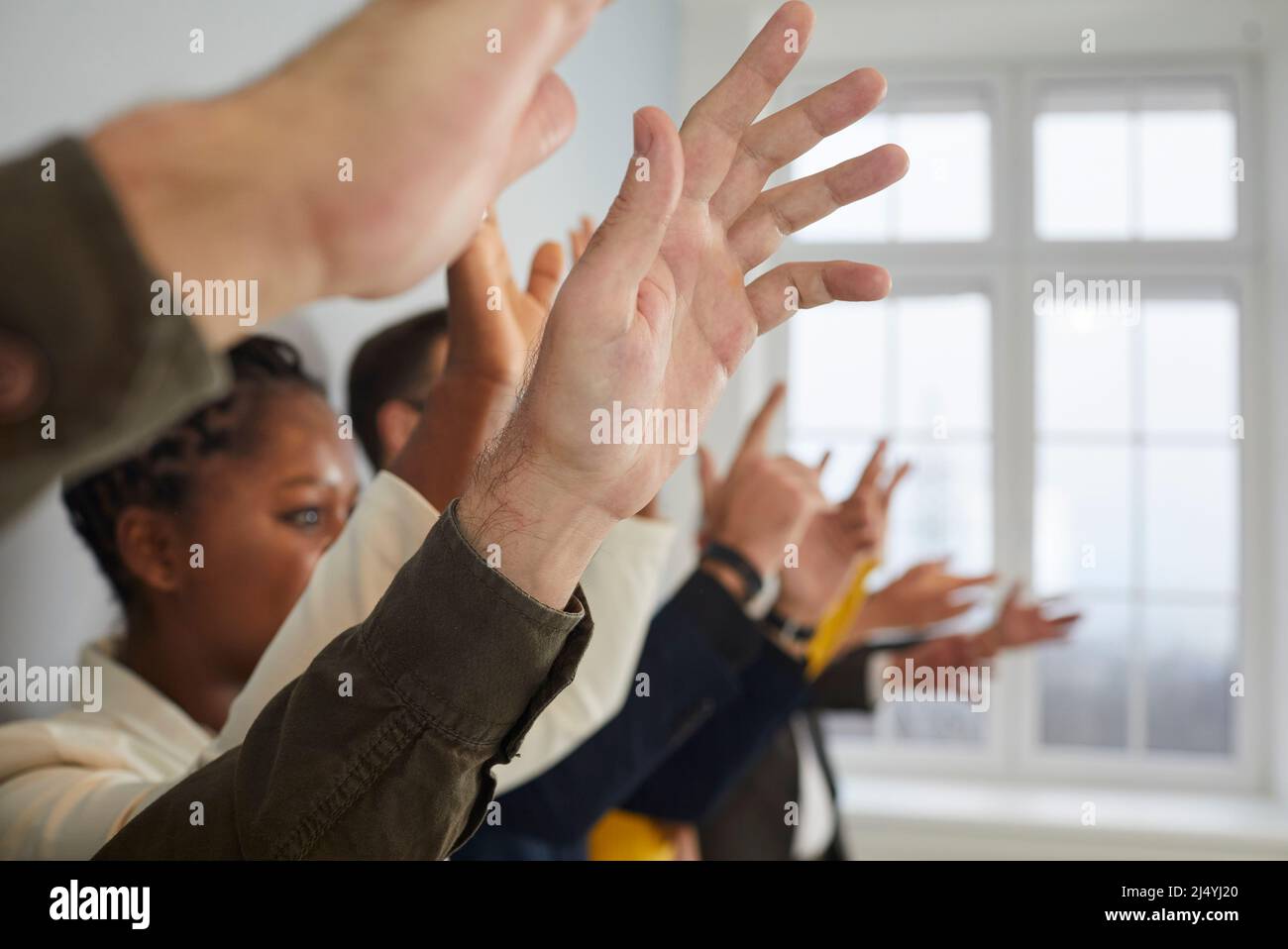 Diverse crowd of people raising their hands to ask questions at public conference Stock Photo