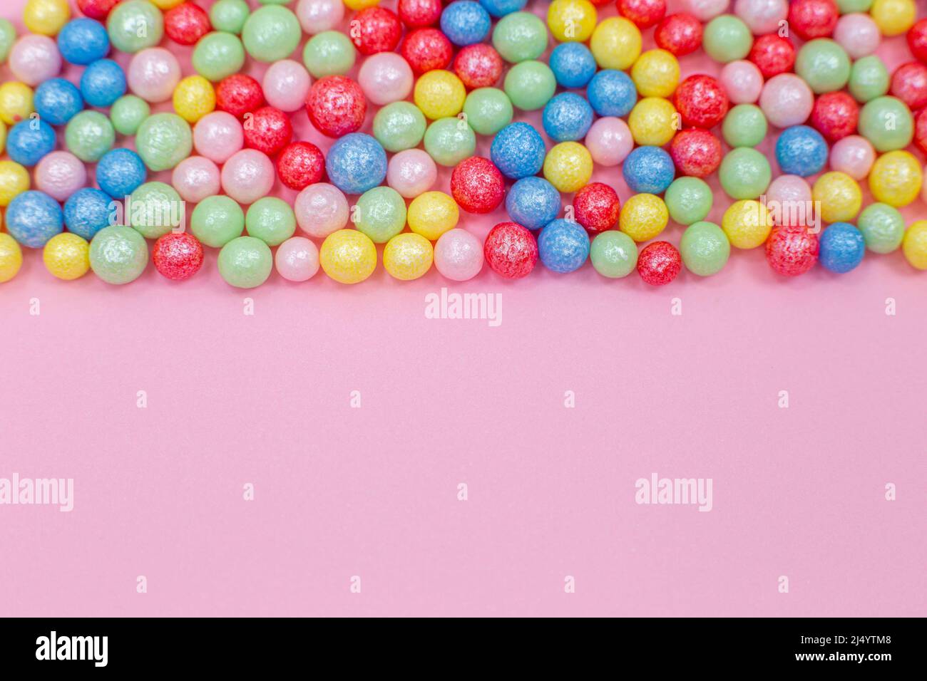 Multi-colored round glossy balls of sugar confectionery topping lie at the top on a pink background. Stock Photo