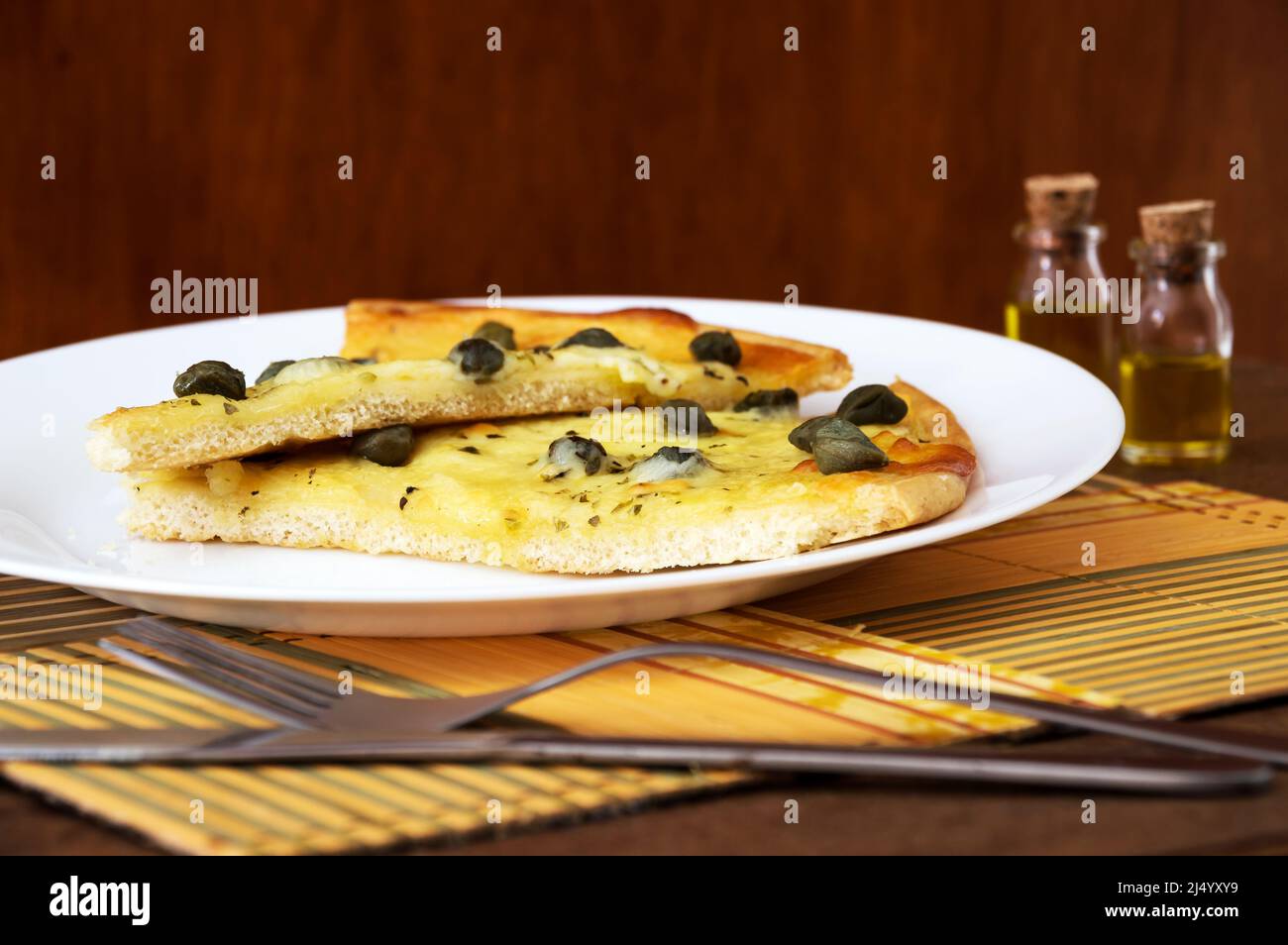 Two slices of caper pizza inside a white plate on top of bamboo pillow