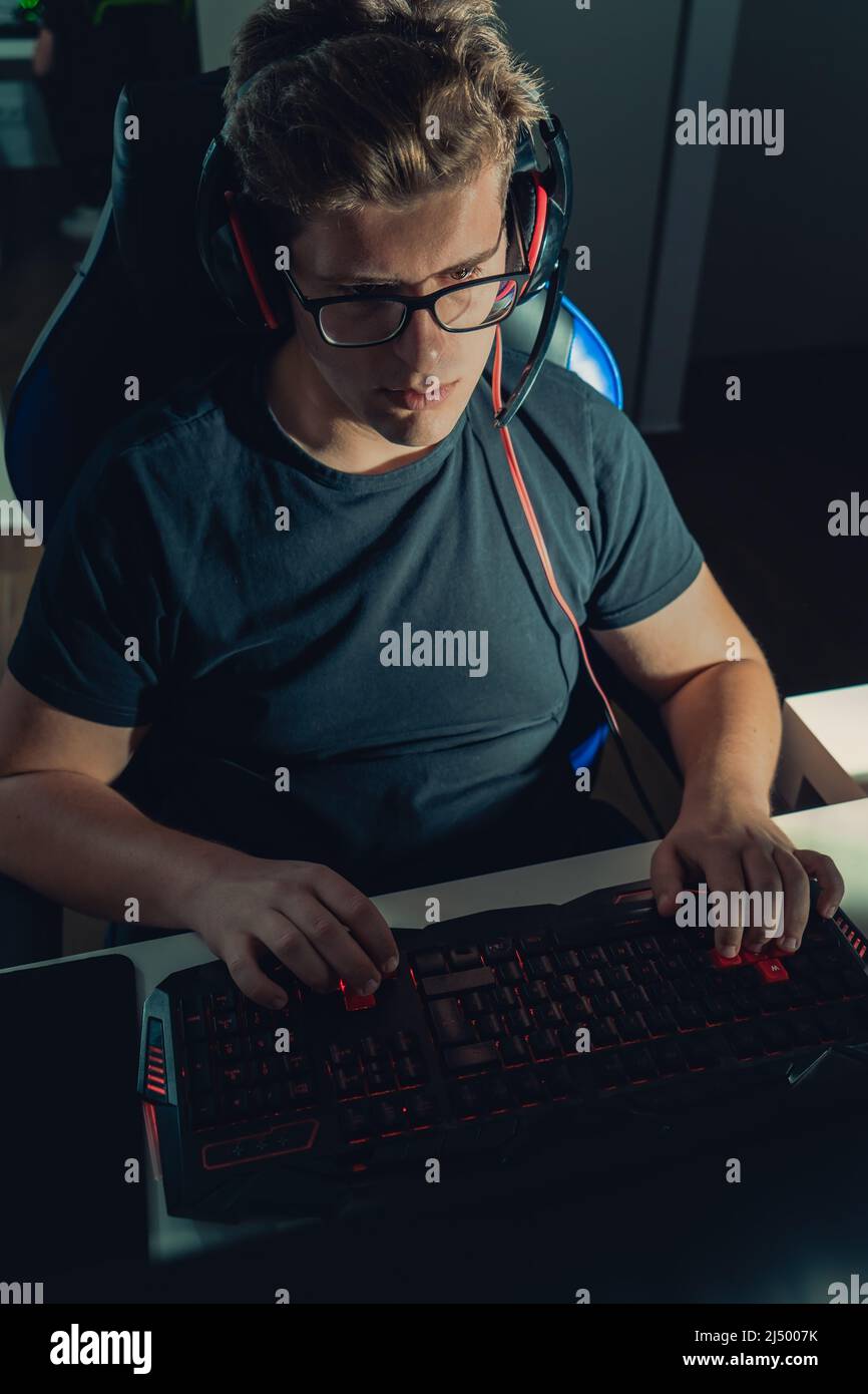 Young blond guy playing video games, playing on his laptop in the dark illuminated by the screen. Stock Photo