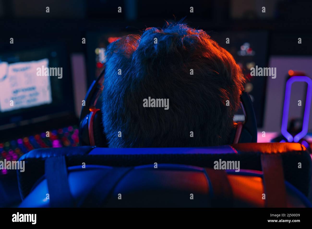 Silhouette of the back of a young man addicted to video games playing on a computer with headphones.  Stock Photo