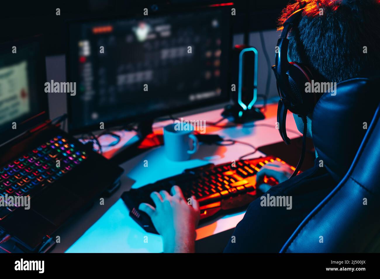 Young man addicted to video games playing on a computer with headphones. Young gamer illuminated with coloured lights Stock Photo