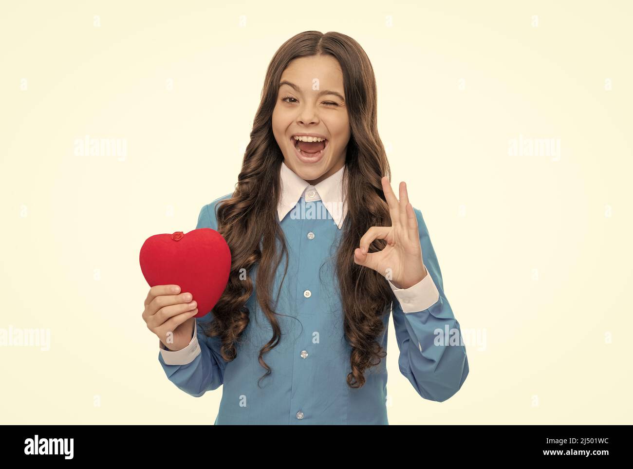 Playful girl hold red valentines heart showing OK hand gesture isolated on white, approval. Stock Photo