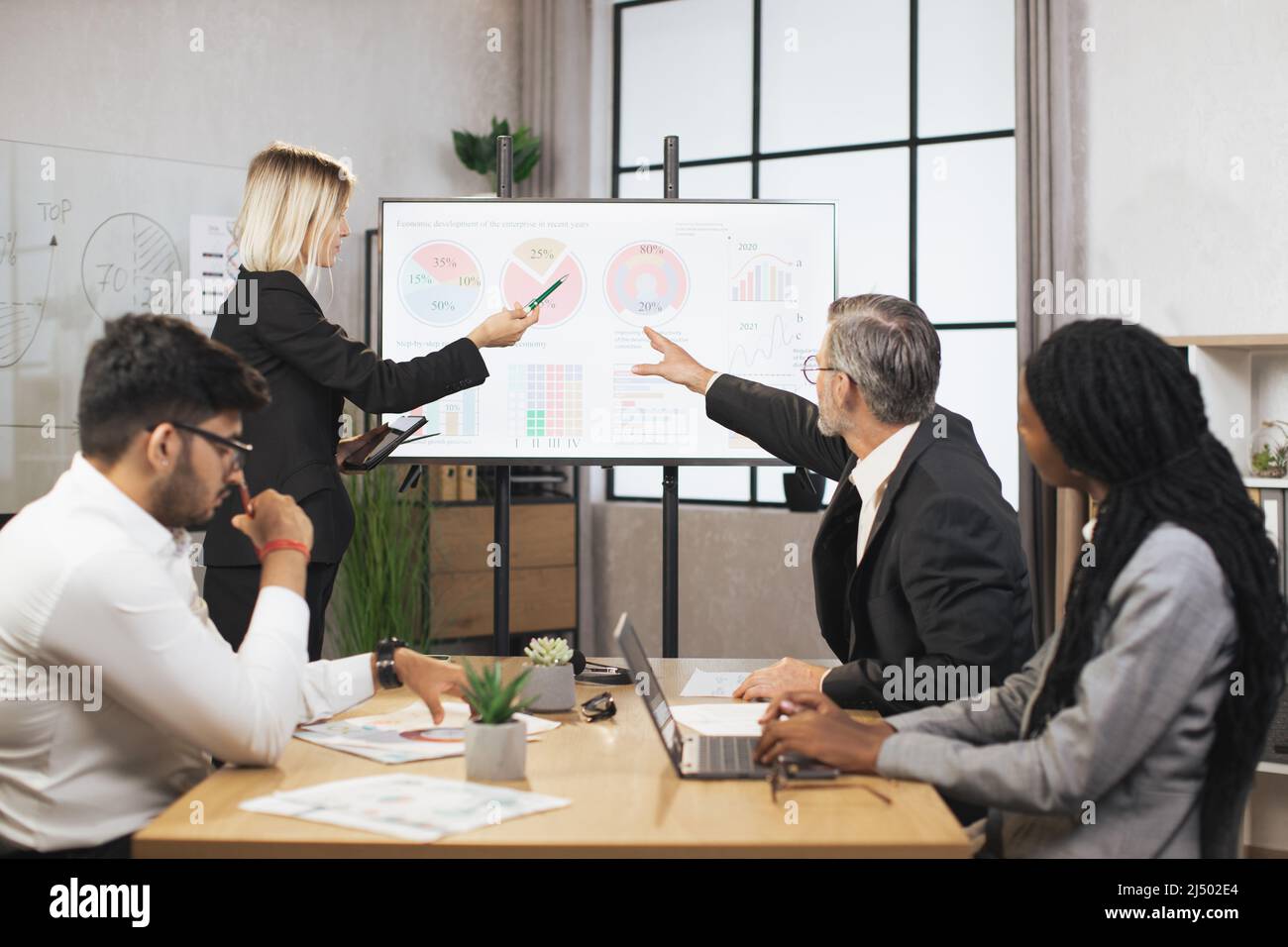 Group of diverse multiethnic businesspeople, sitting at the table in office and listening the marketing and financial report from their young confident caucasian female and mature male colleague Stock Photo
