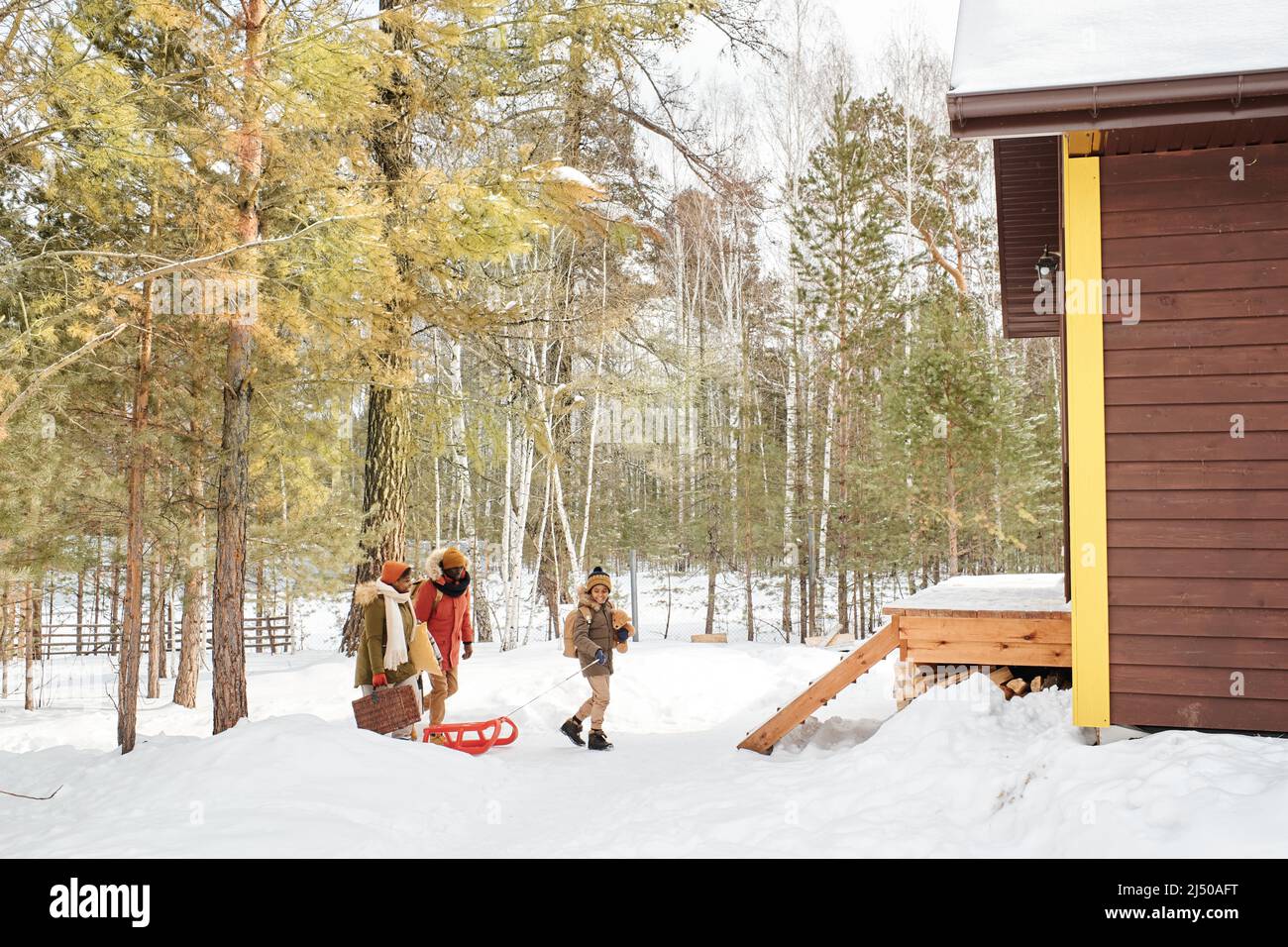 Contemporary black family of three in winterwear moving towards their country house located in the forest to spend weekend there Stock Photo