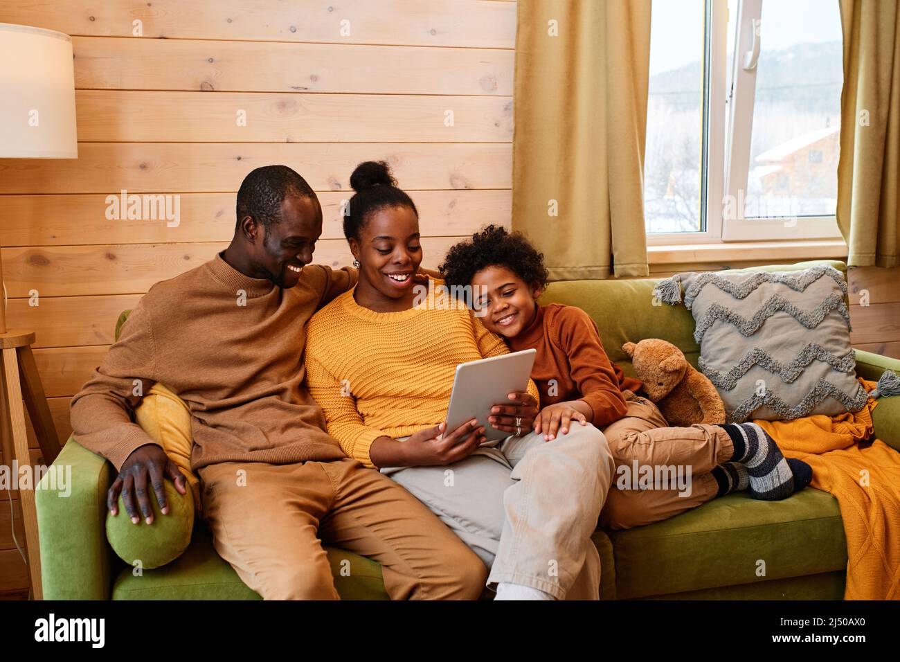 Young contemporary family communicating in video chat while relaxing on comfortable couch in living room of their country house Stock Photo