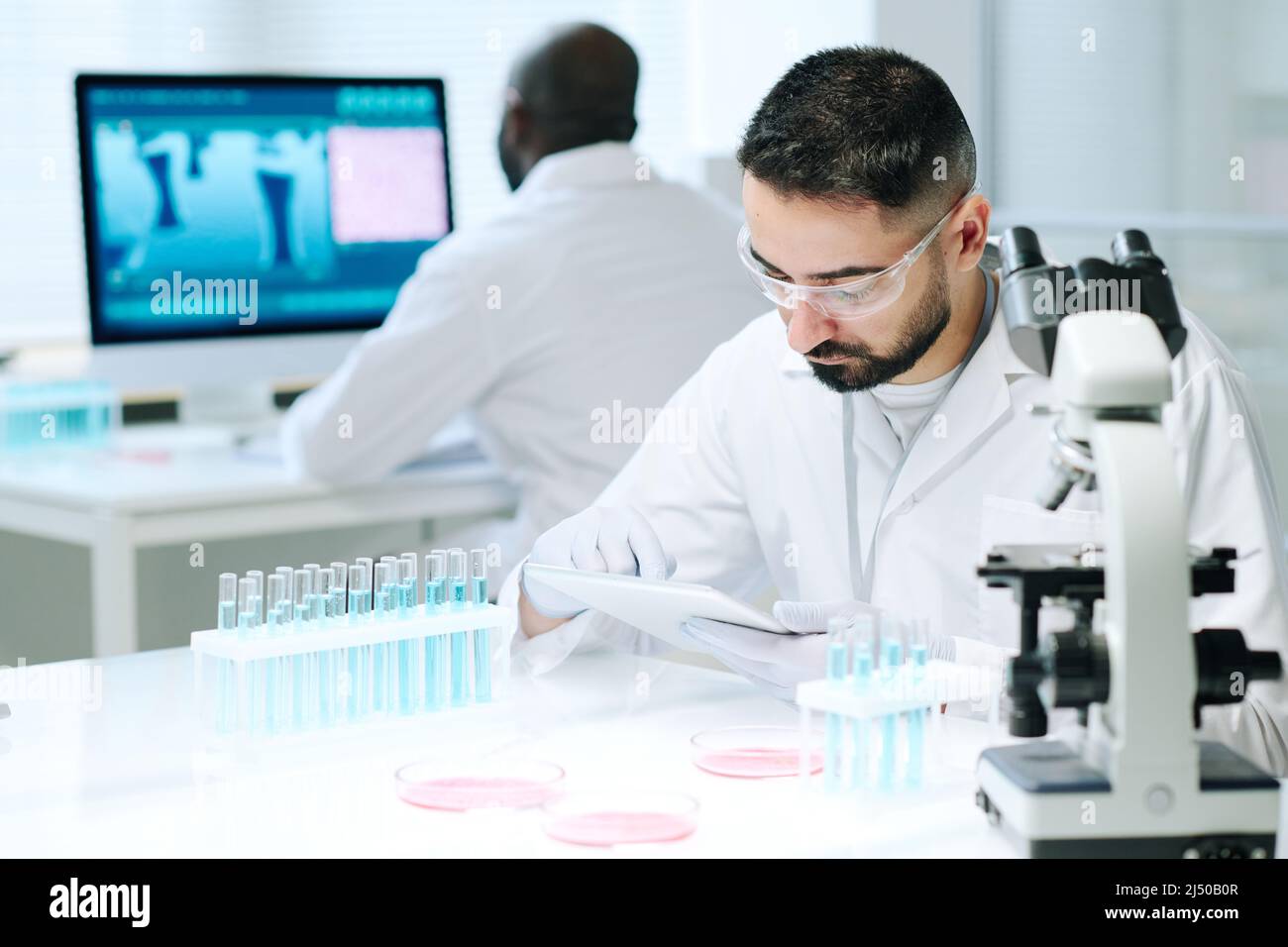 Contemporary young male scientist in workwear using digital tablet while searching for online data about new biotechnologies Stock Photo