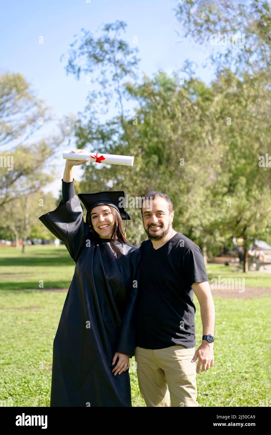 Young girl recently graduated, dressed in cap and gown, with her degree in her hand, celebrating with her family on the university campus. Very happy Stock Photo