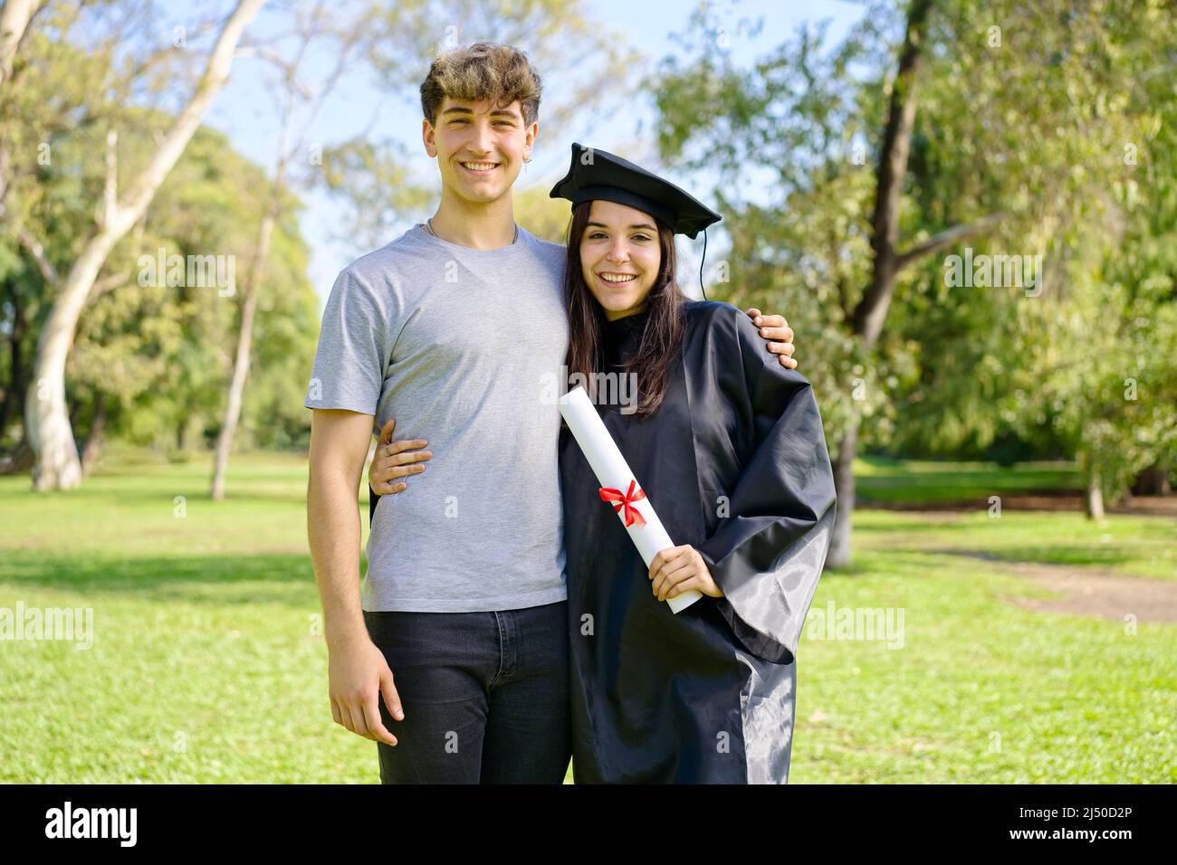 Young girl recently graduated, dressed in cap and gown, with her degree in her hands, celebrating with her family on the university campus. Very happy Stock Photo