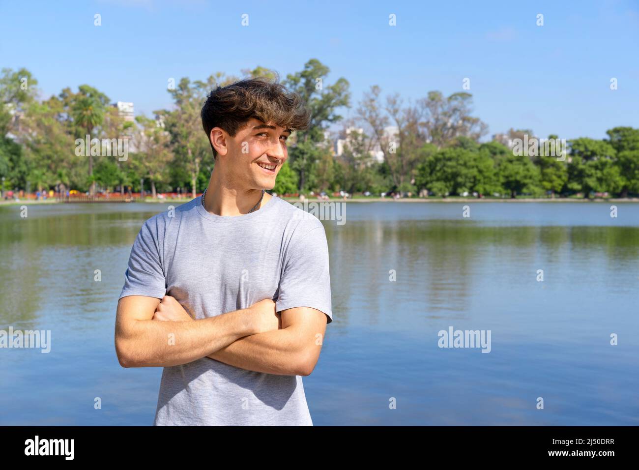 Portrait of confident young blond man with crossed arms looking at camera, summer lake background. Copy space Stock Photo