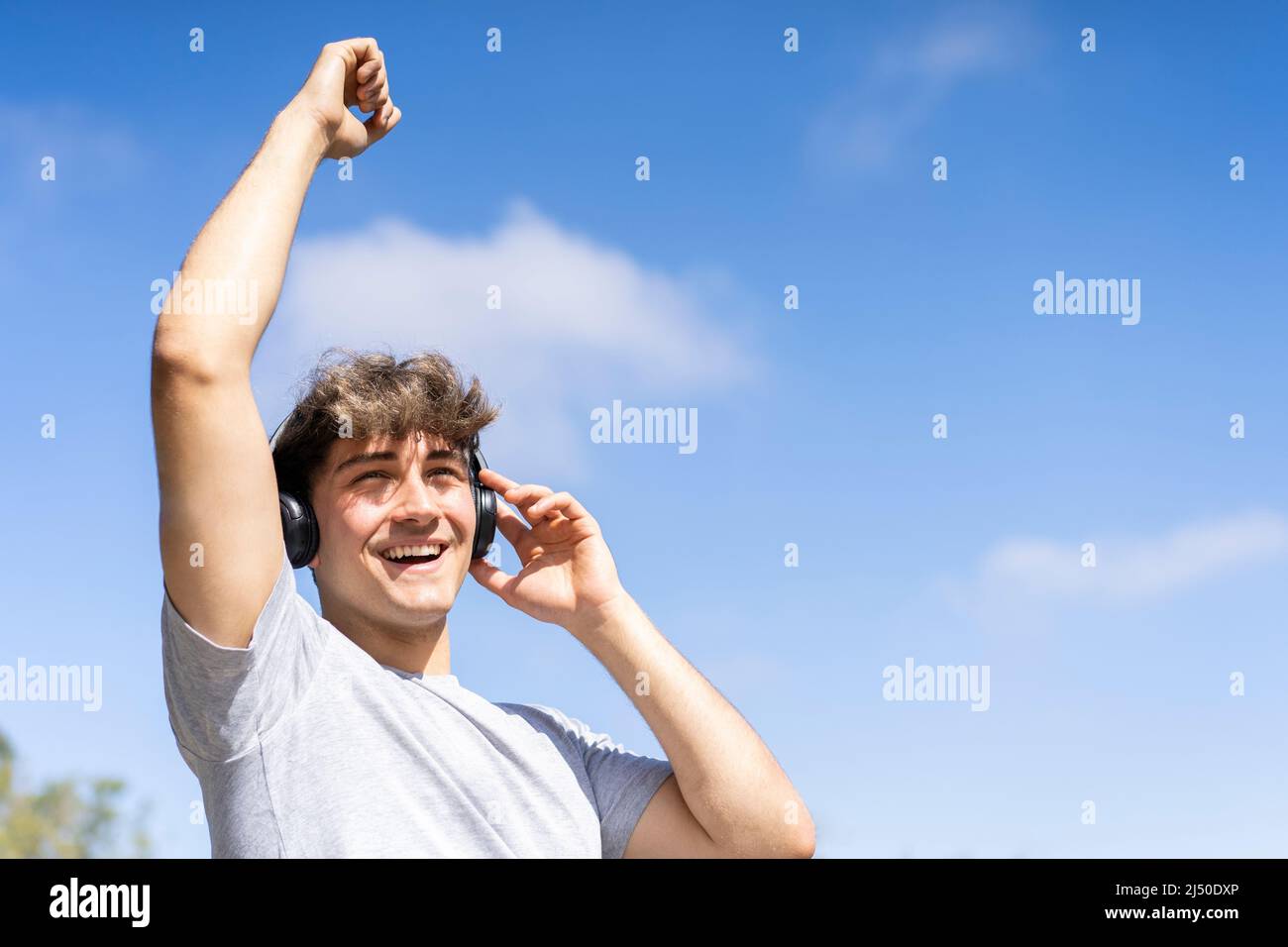 Young man listening to music outdoors with bluetooth headphones. Expression of happiness, winning attitude. Stock Photo