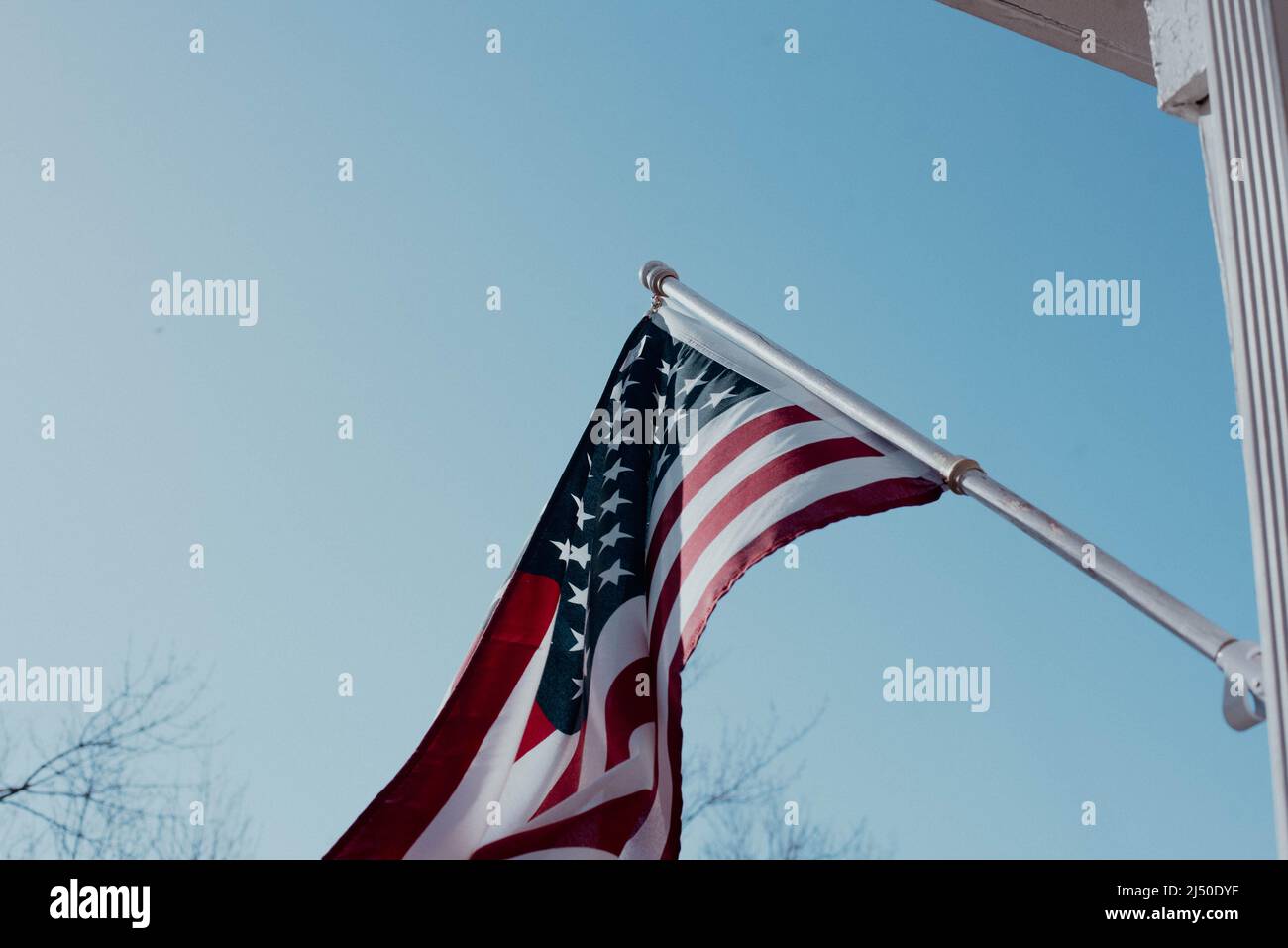 An American flag hangs outside a home against a blue sky. Stock Photo