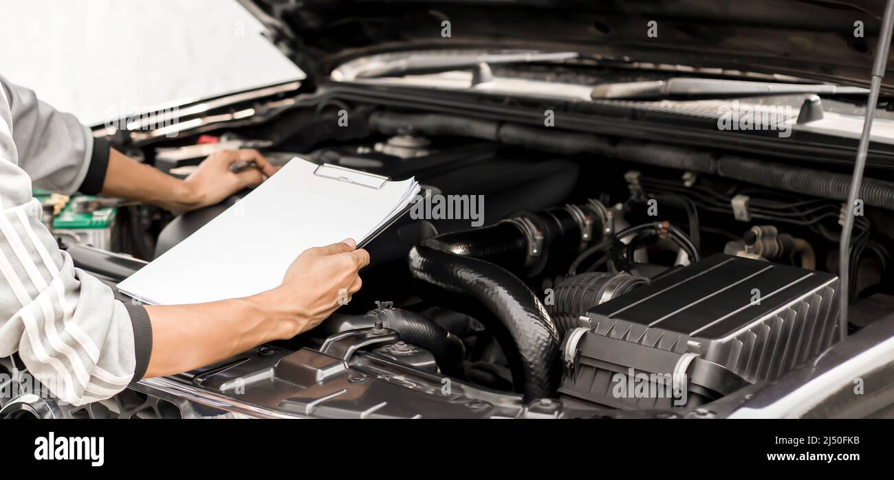 Automobile mechanic repairman checking a car engine with inspecting writing to the clipboard the checklist for repair machine. Stock Photo