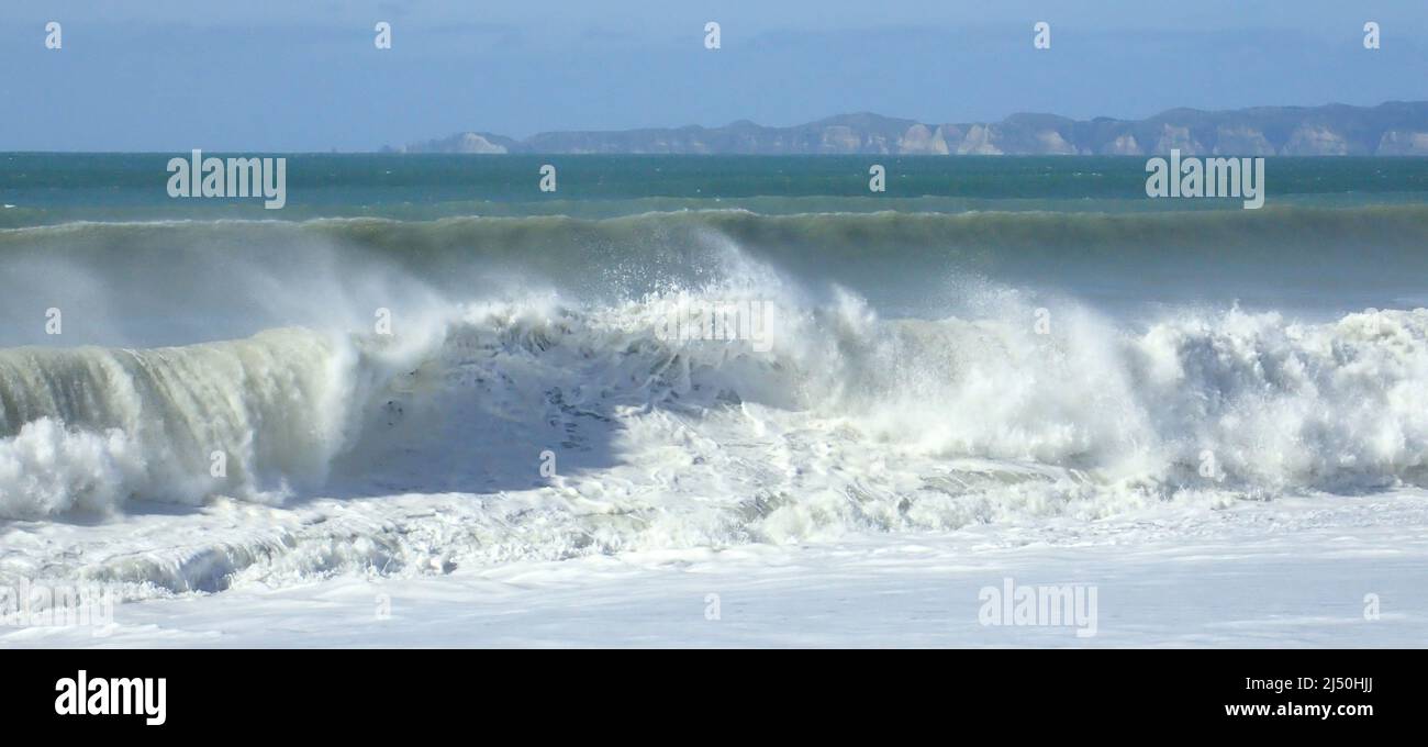 Pacific Ocean waves crash onto the beach at Napier after a storm; Cape Kidnappers in the background Stock Photo