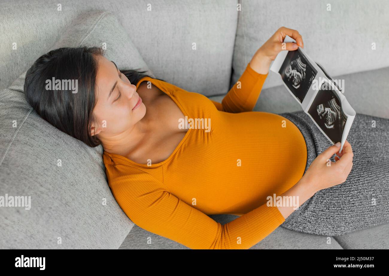 Baby ultrasound scan. Pregnant Asian woman holding hospital picture result from health checkup with small belly happy of first pregnancy Stock Photo