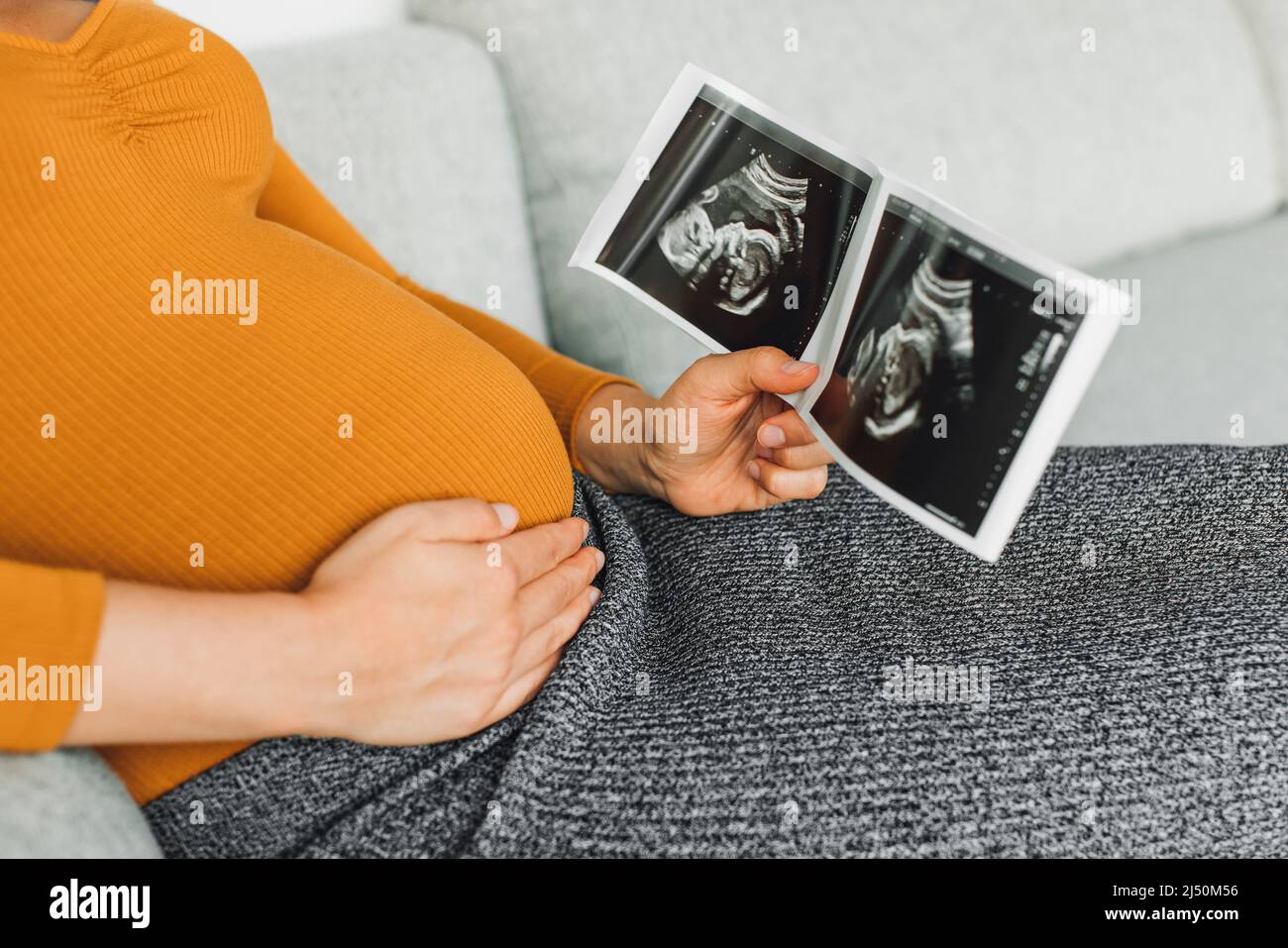 Pregnant woman looking at first ultrasound photo of her baby, caressing her belly happily awaiting the birth of her child. First trimester pregnancy Stock Photo