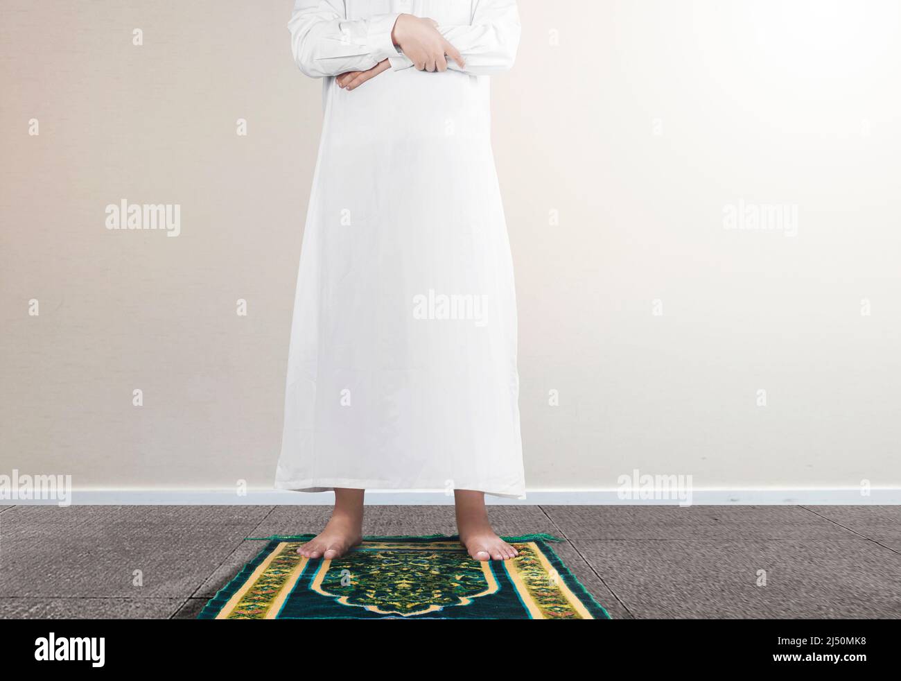 Close up view of a Muslim man in a praying position (salat) on a prayer rug with white wall