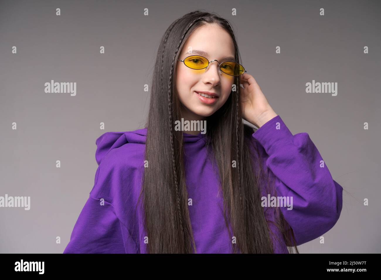 Portrait cute teenage girl in purple sweatshirt and yellow glasses posing in the studio on a gray background. Caucasian girl raotae on camera Stock Photo