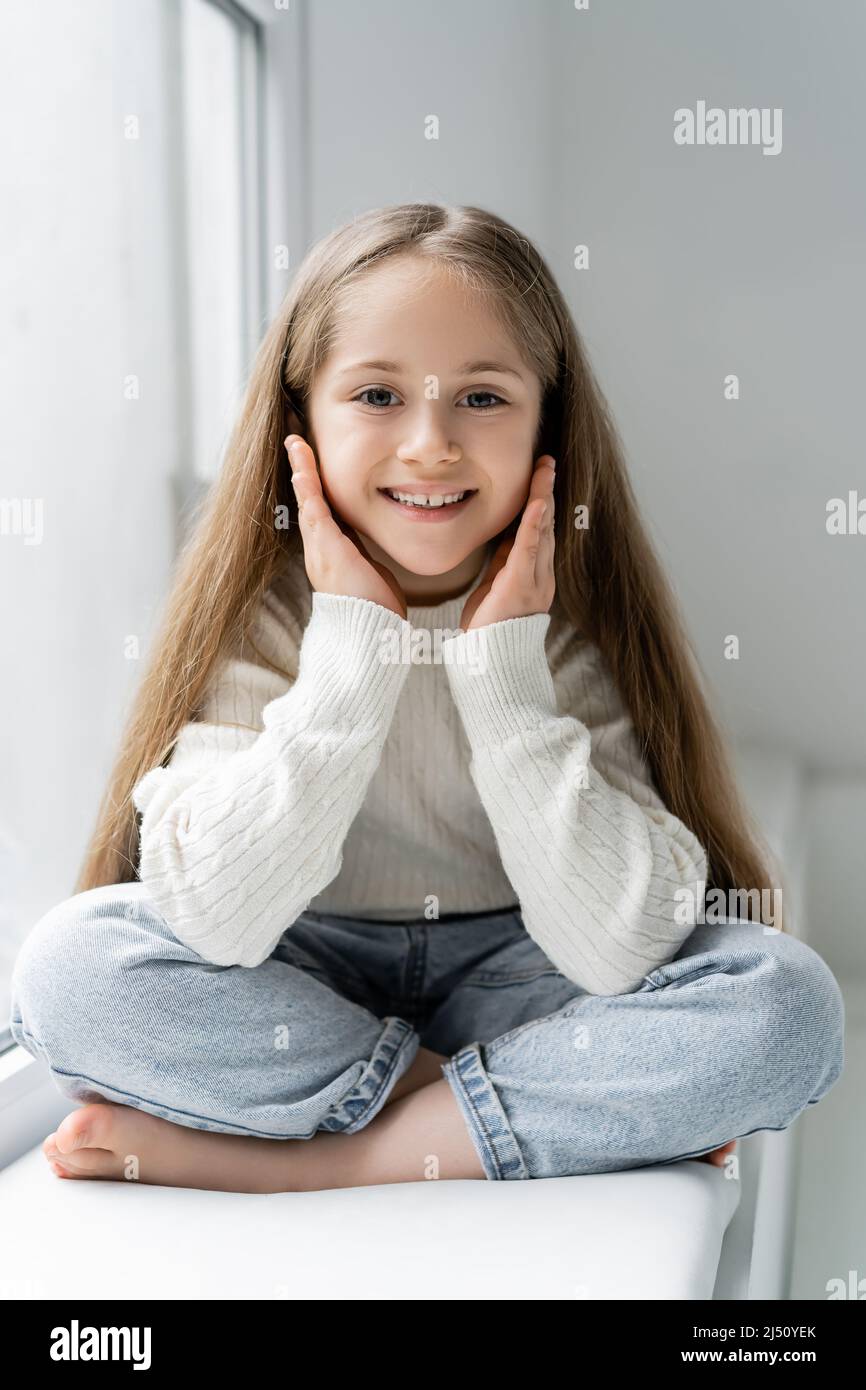 cheerful barefoot girl looking at camera while sitting with crossed
