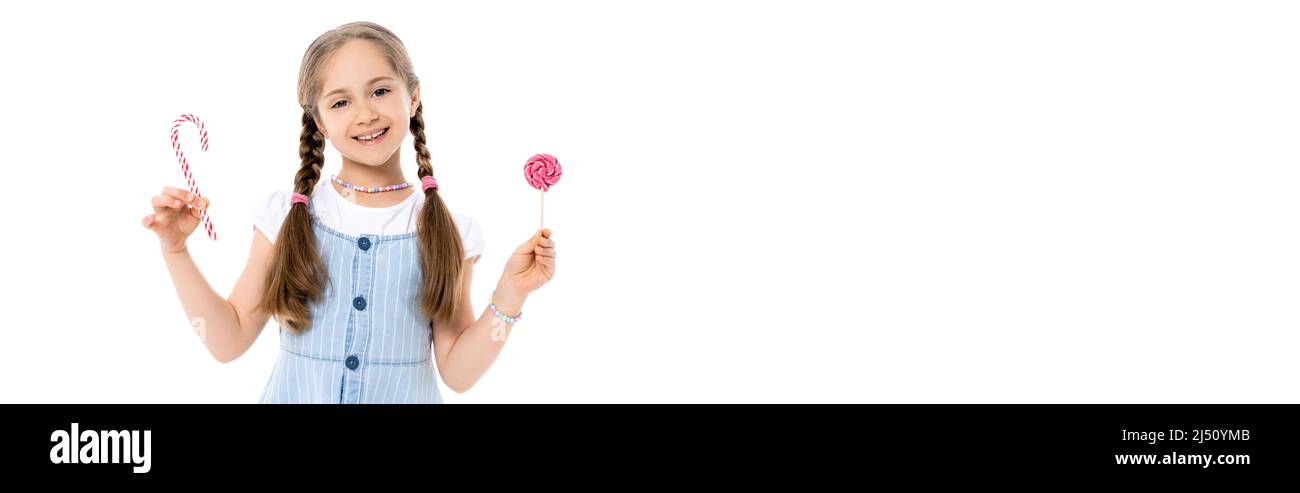 girl in colorful necklace holding lollipop and candy cane isolated on white, banner Stock Photo