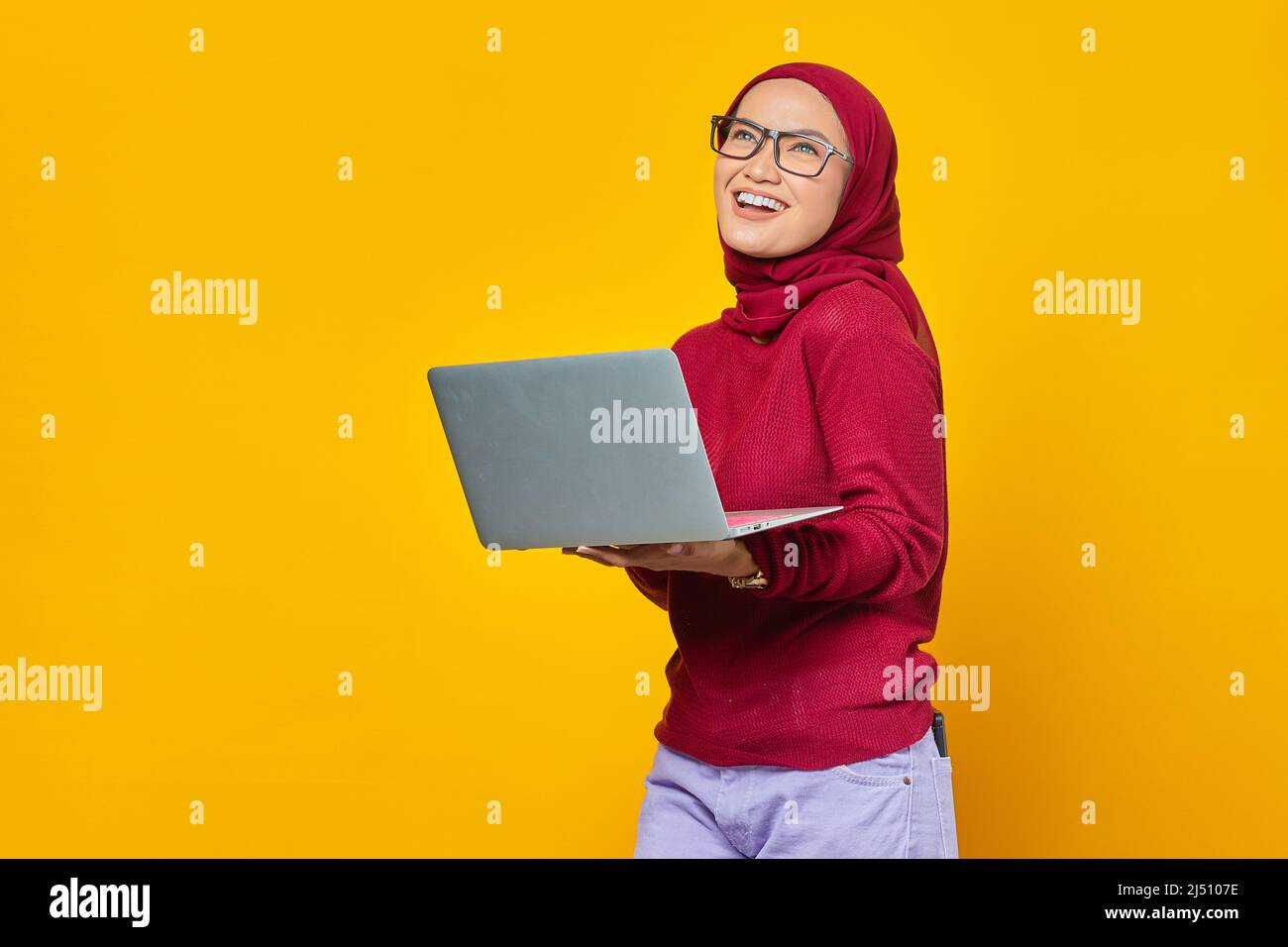 Portrait of smiling Asian woman holding laptop and looking up over ...