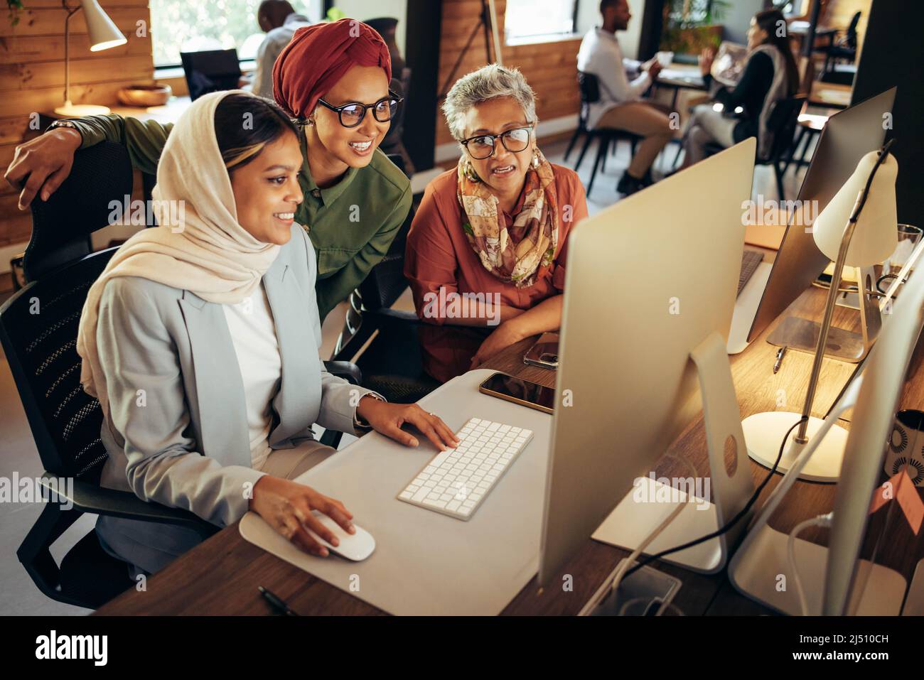 Happy businesswomen working as a team in a modern co-working office. Group of multicultural businesswomen having a discussion while looking at a compu Stock Photo