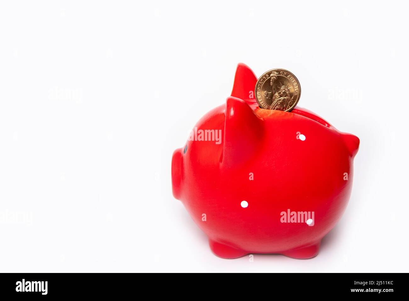 Coin 1 dollar in a hole in a red piggy bank on a white background. Savings concept. The stability of the national currency. Wealth concept. Stock Photo