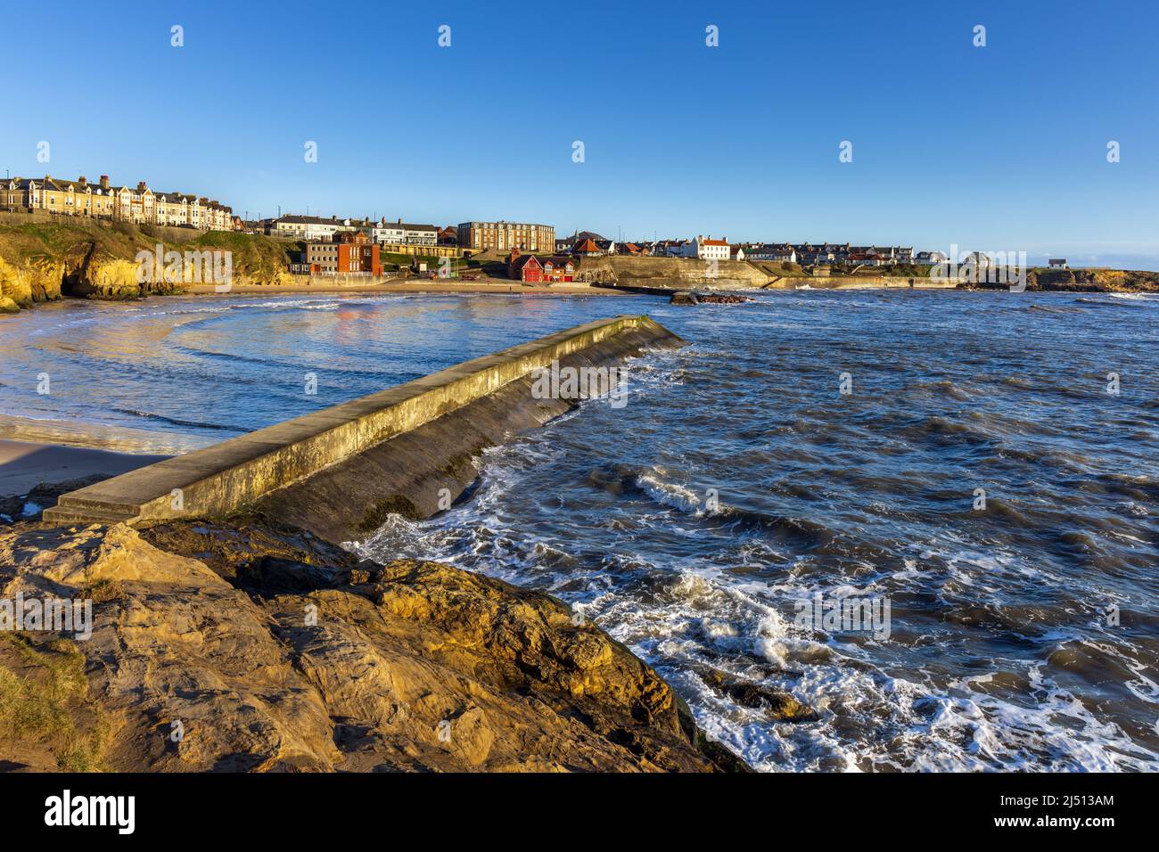 Early morning sun shines on the harbour wall breakwaters at Cullercoats Bay, North Tyneside, Uk Stock Photo