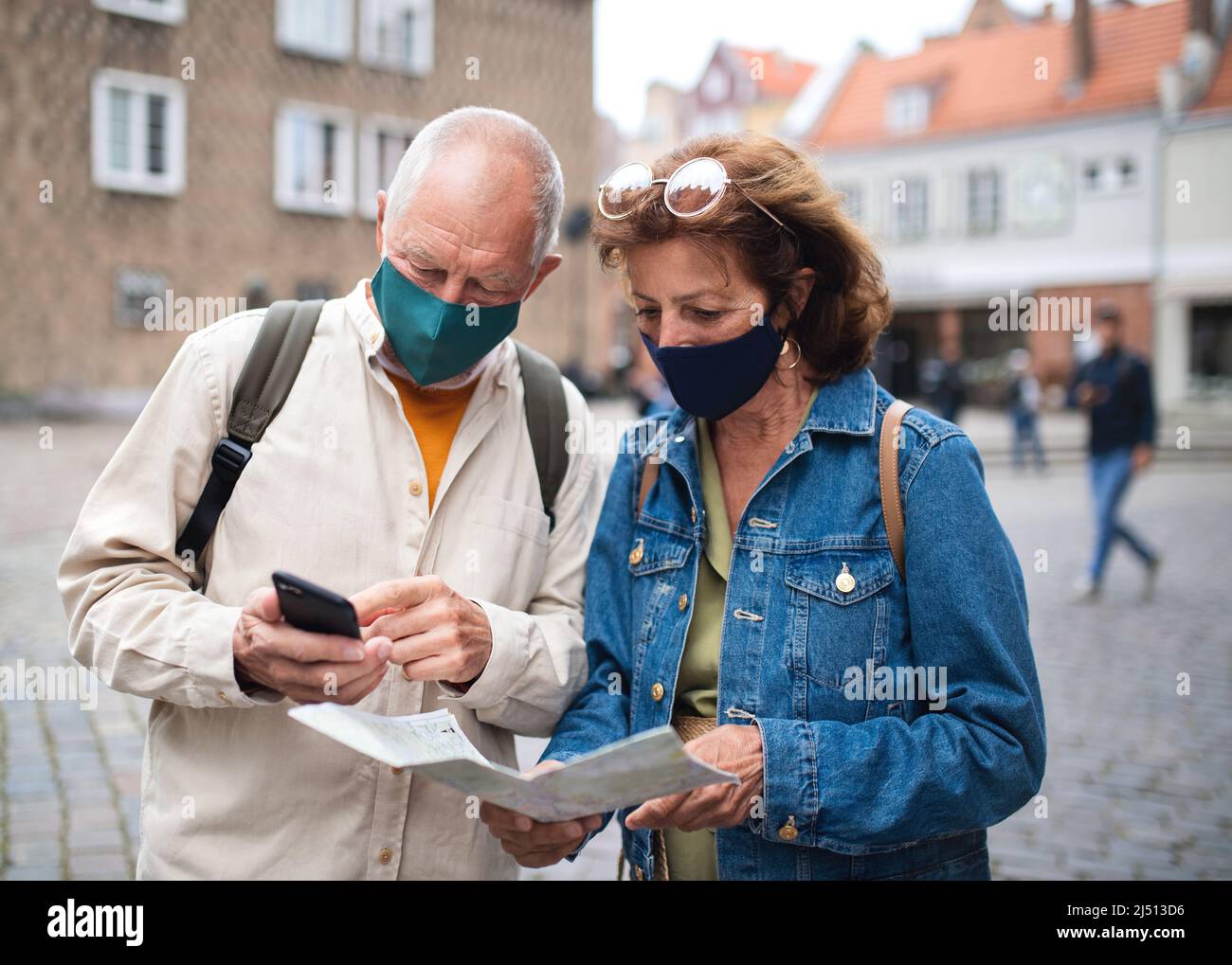 Senior couple tourists with face masks using map outdoors in town ...
