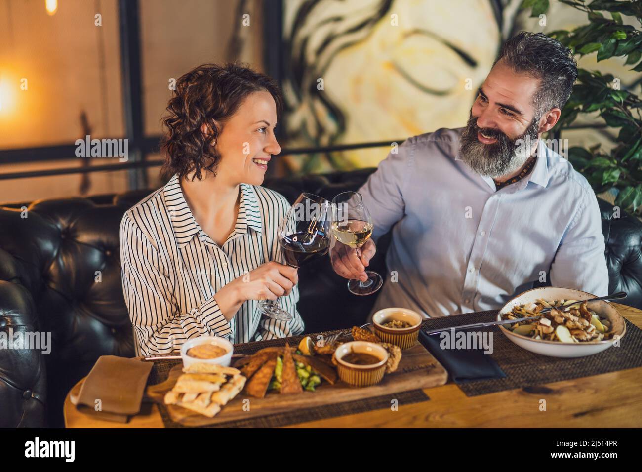 Happy couple is sitting at restaurant. They are having dinner with wine and spending nice time together. Stock Photo