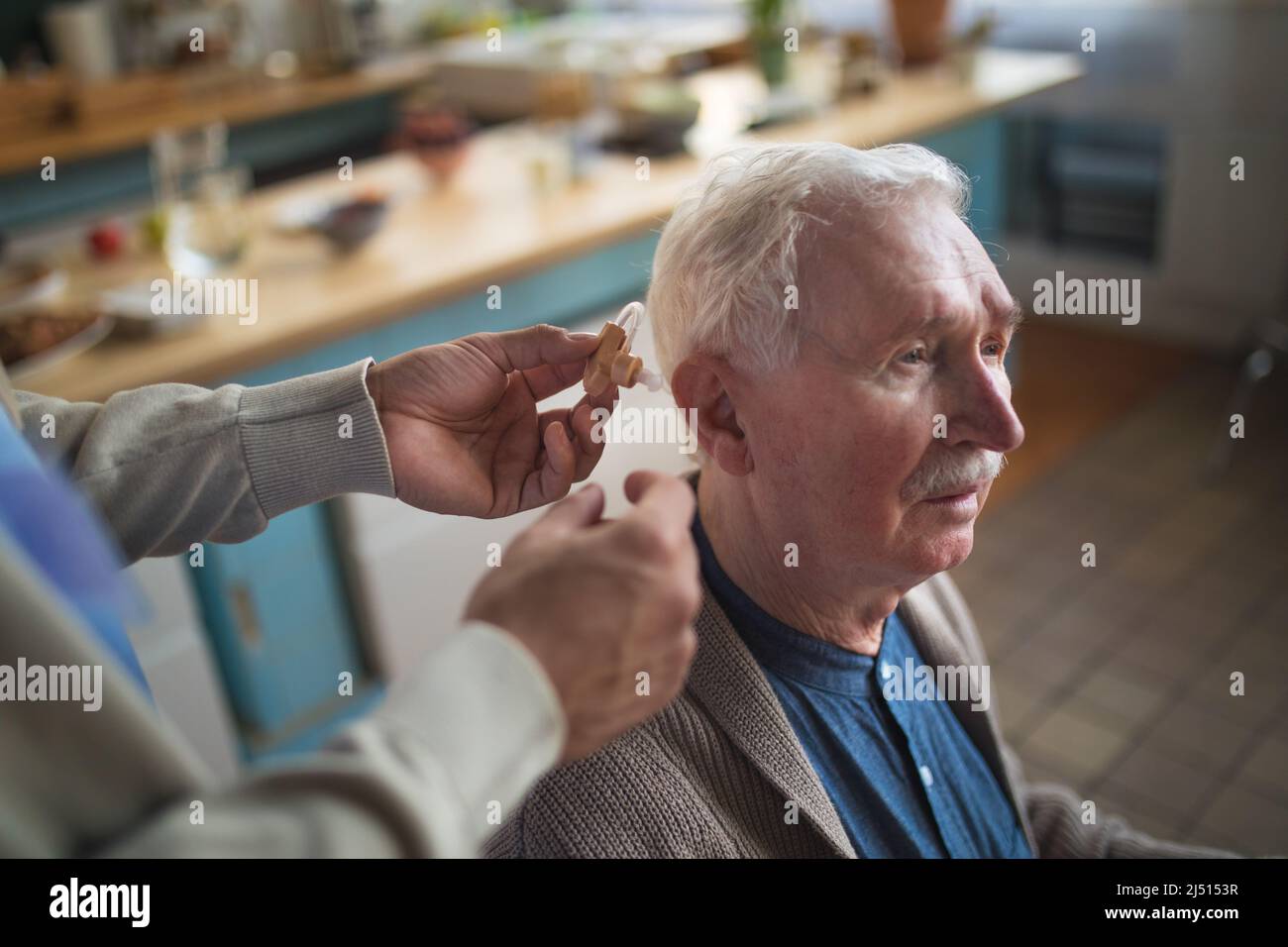 Caregiver helping senior man to insert hearing aid in his ear. Stock Photo
