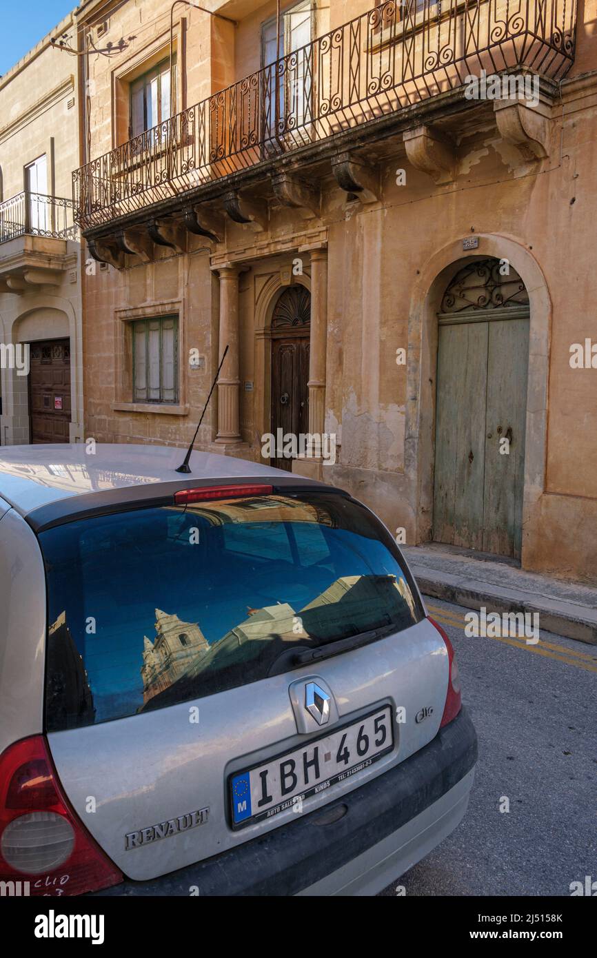 A street in Mellieha with the parish church reflected in a car window, Malta Stock Photo