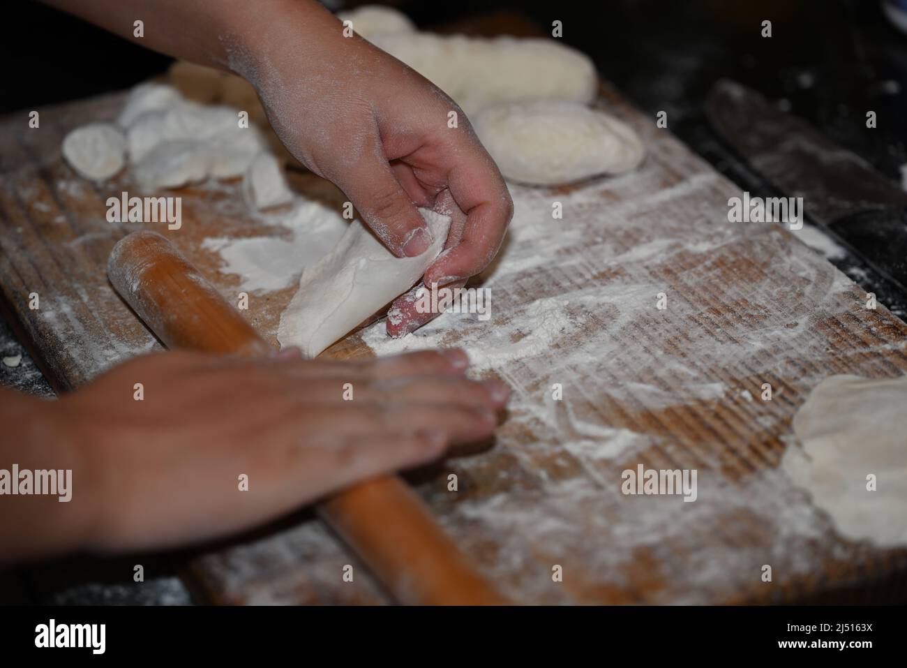 Dough to be used as a wrapper for Chinese dumplings being pulled away from a rolling pin, on a