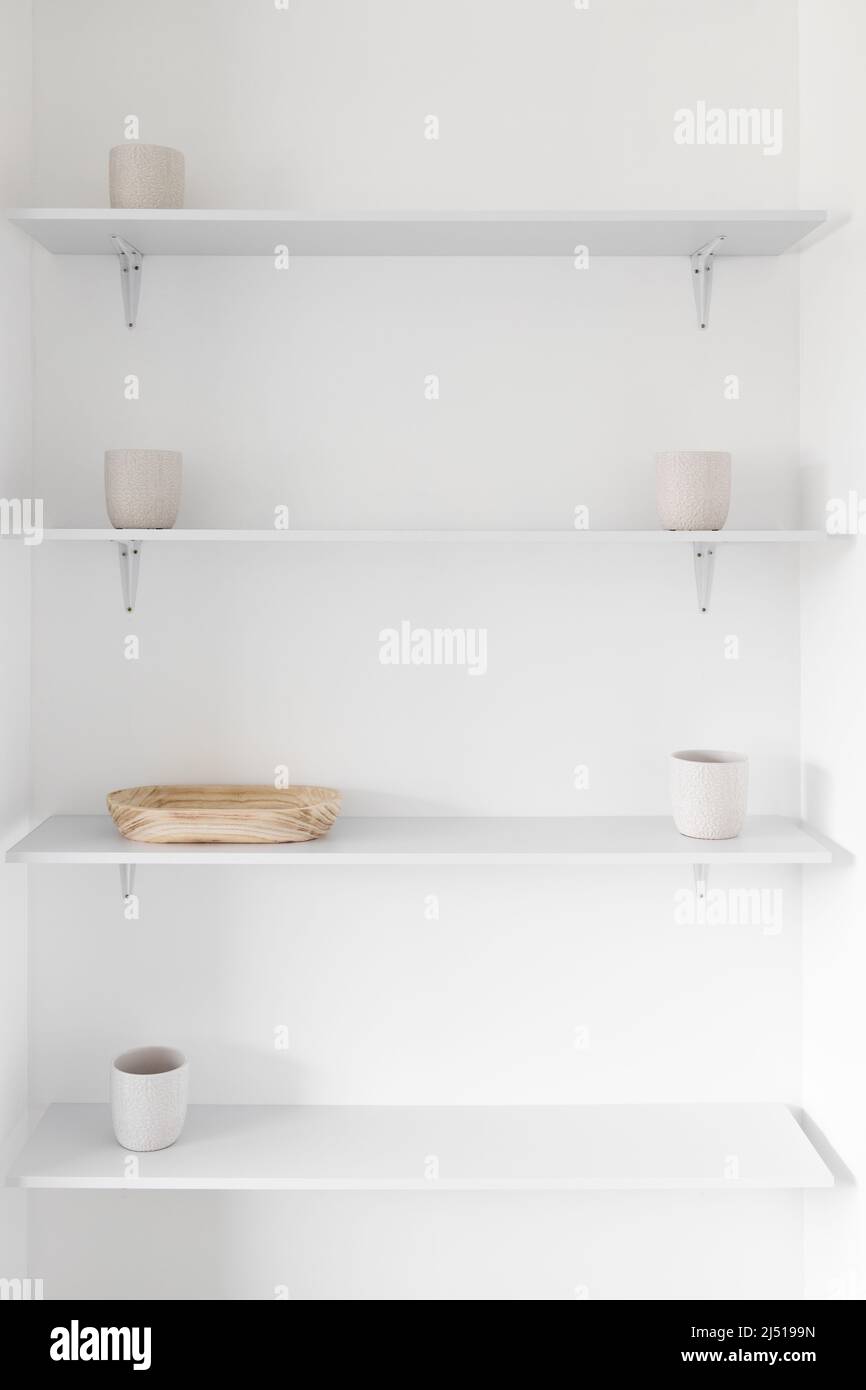 minimalist white wall with shelves in a niche with white plant pots and wooden tray, concept of