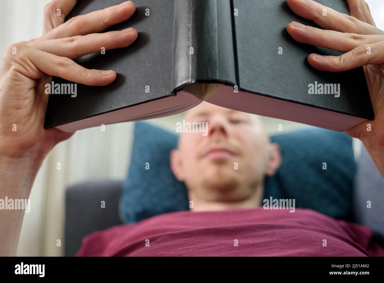 Bald hairless man reading book lying on couch Stock Photo
