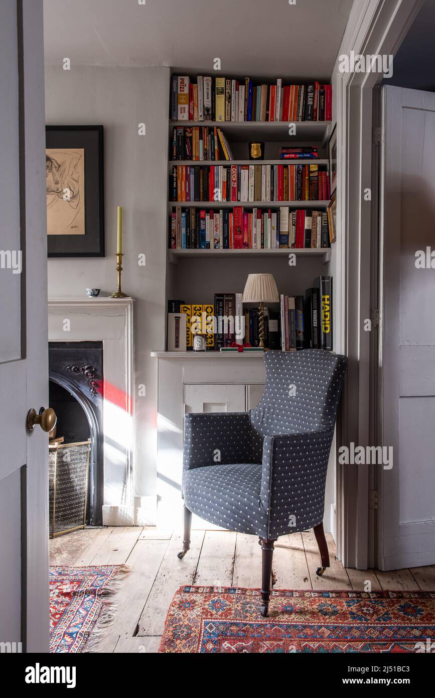 Upholstered chair with Edwardian fireplace and bookshelves in Grade II listed 1820s London cottage, UK Stock Photo