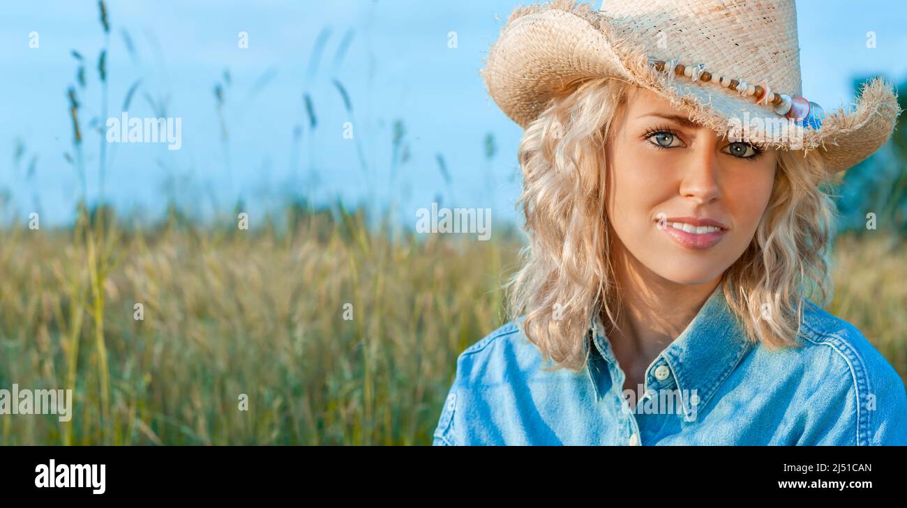 Outdoor portrait of smiling and happy, beautiful young female teenager with blonde hair wearing denim shirt and cowboy hat in a field and evening suns Stock Photo