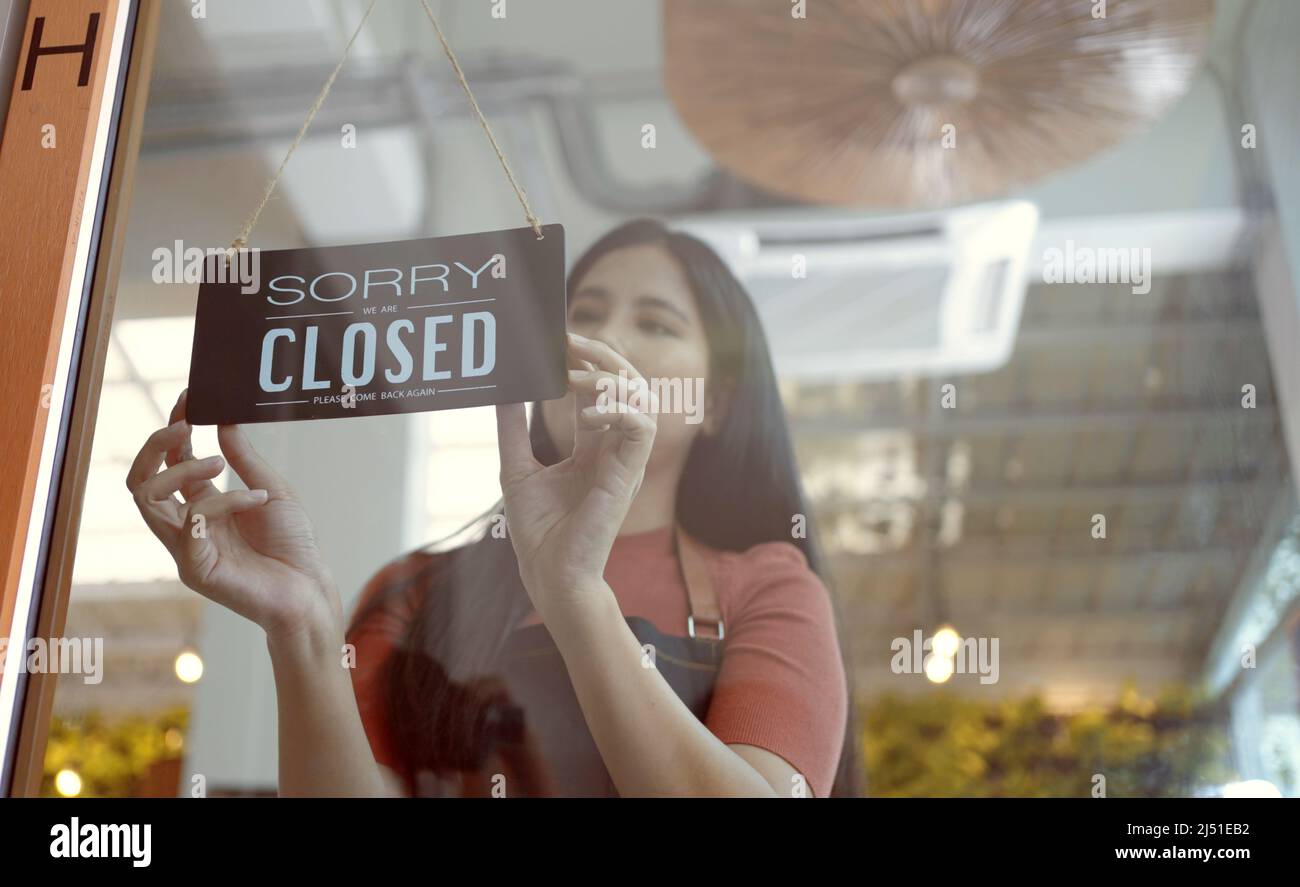 Owner coffee shop woman hand flip the sign to closed the shop.closed sign hanging on the glass door. Stock Photo