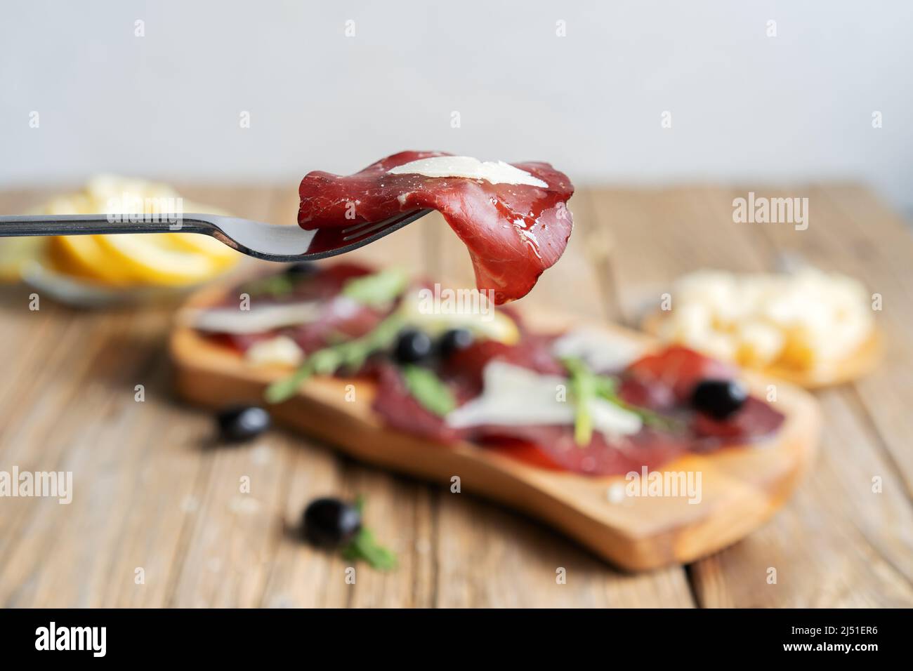 Jerky meat bresaola on the fork with lemons, grana, olives and arugula Stock Photo
