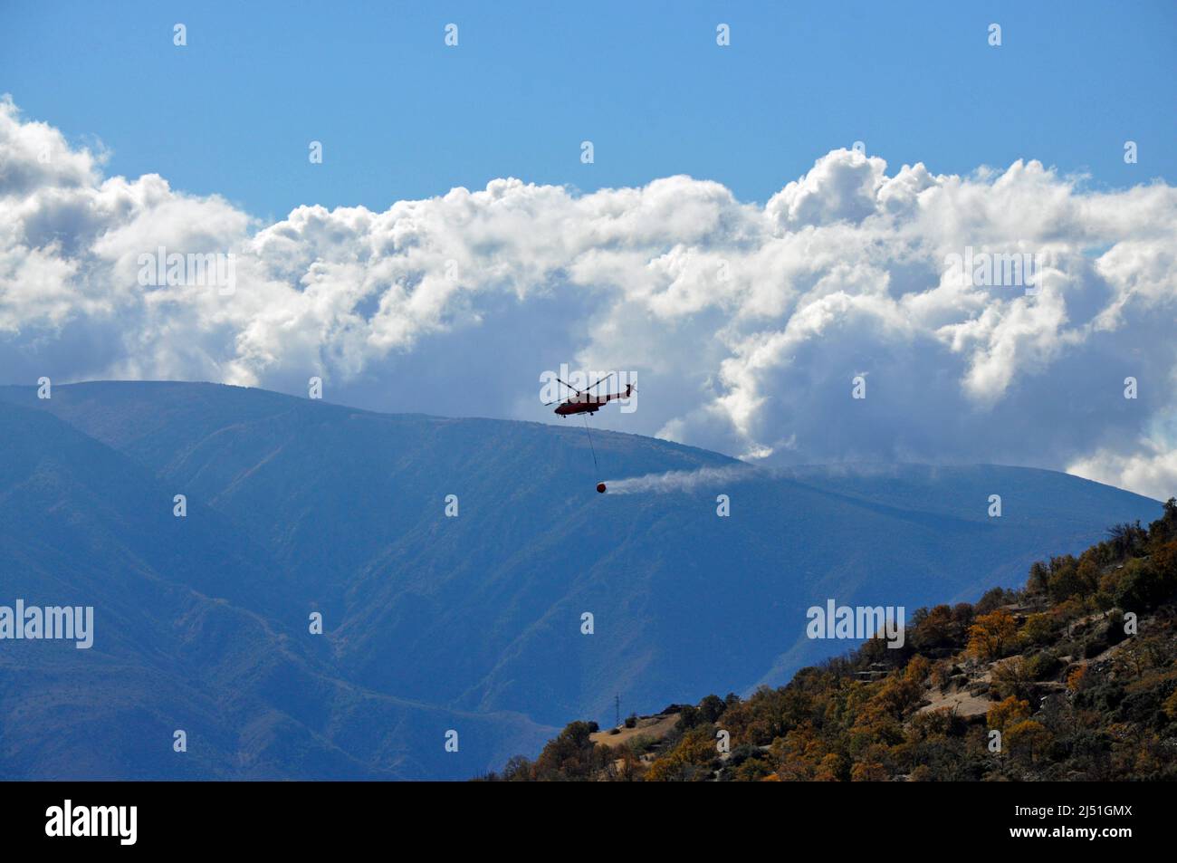 A helicopter water bombing a wild fire near the village of Capileira in