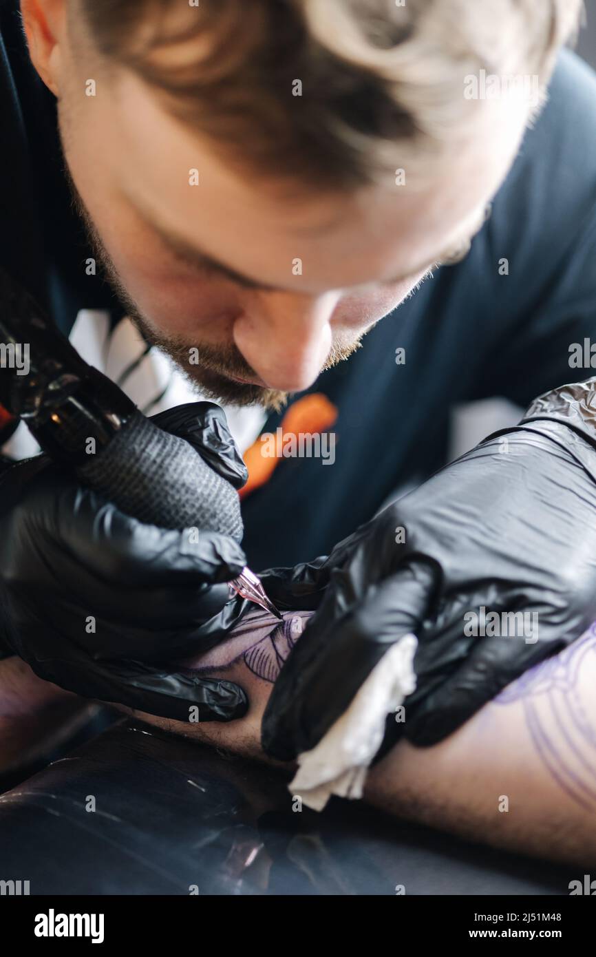 Close up of a young professional tattoo master introduces black ink into the skin using needle from a wireless tattoo machine. Tattoo on hand. Stock Photo