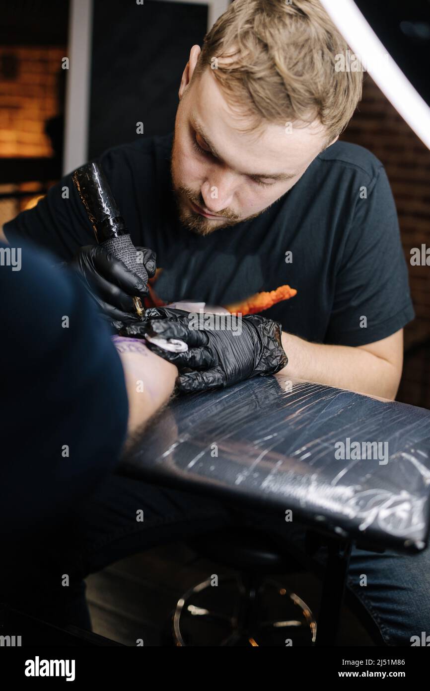 Tattoo master is tattooing a man's hand. Wireless tattoo machine, safety and hygiene at work. Close-up of tattoo artist work. Tattoo salon Stock Photo