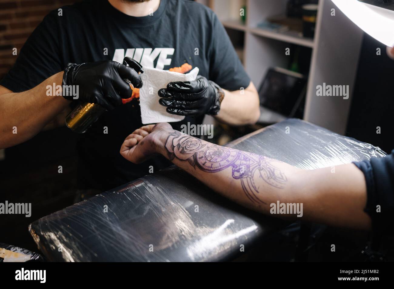 Close up of a young professional tattoo master introduces black ink into the skin using a needle from a tattoo machine. Tattoo on hand Stock Photo