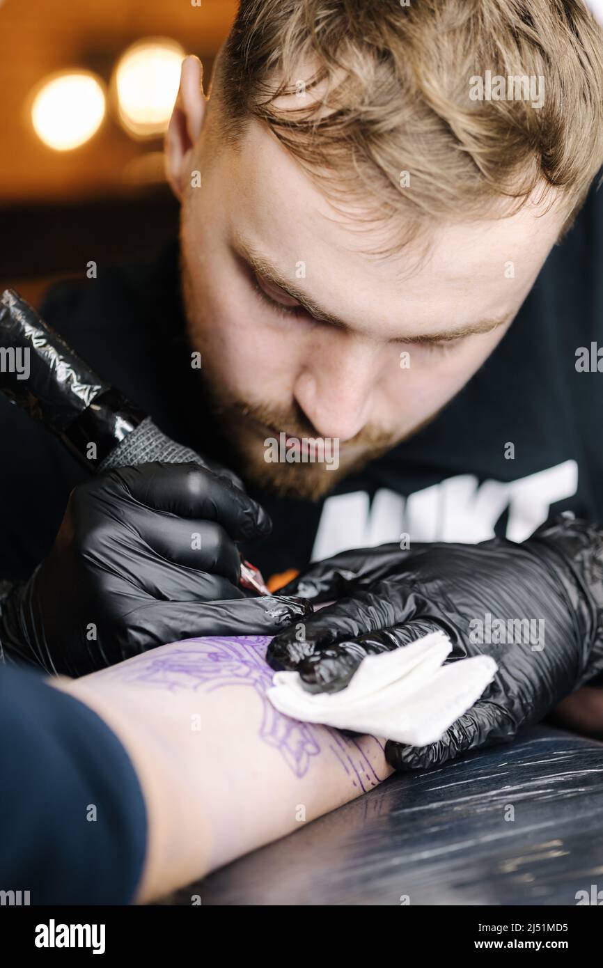 Close up of tattoo master making black tattoo with paint. Master works in black sterile gloves. Young tattoo artist in work Stock Photo