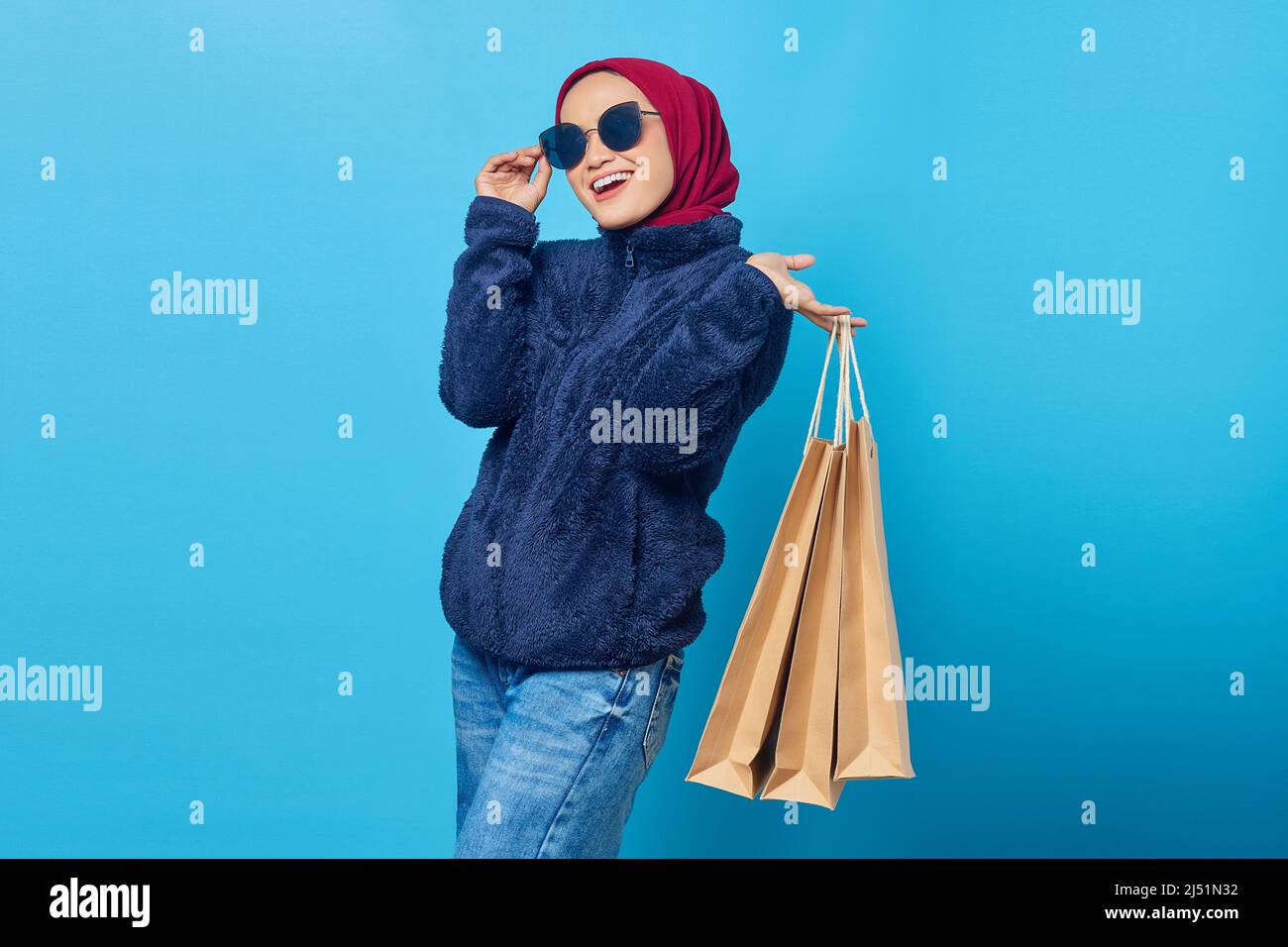 Cheerful young Asian woman wearing sunglasses and holding shopping bags ...