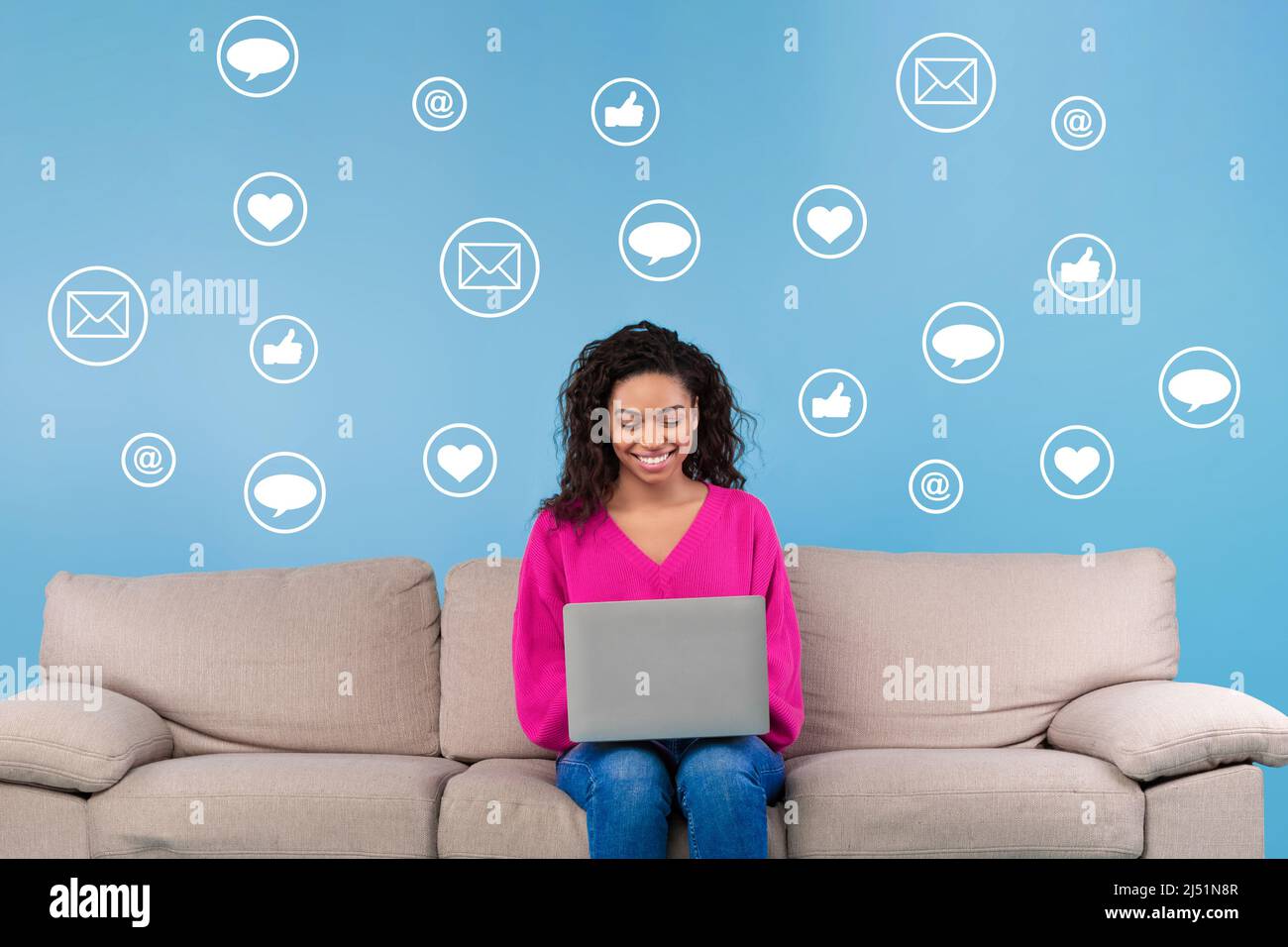 African American Female Using Laptop Computer Sitting On Blue Background Stock Photo