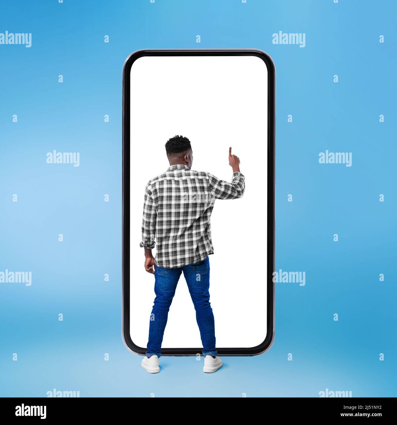 African Man Using Huge Smartphone Over Blue Background, Rear View Stock Photo